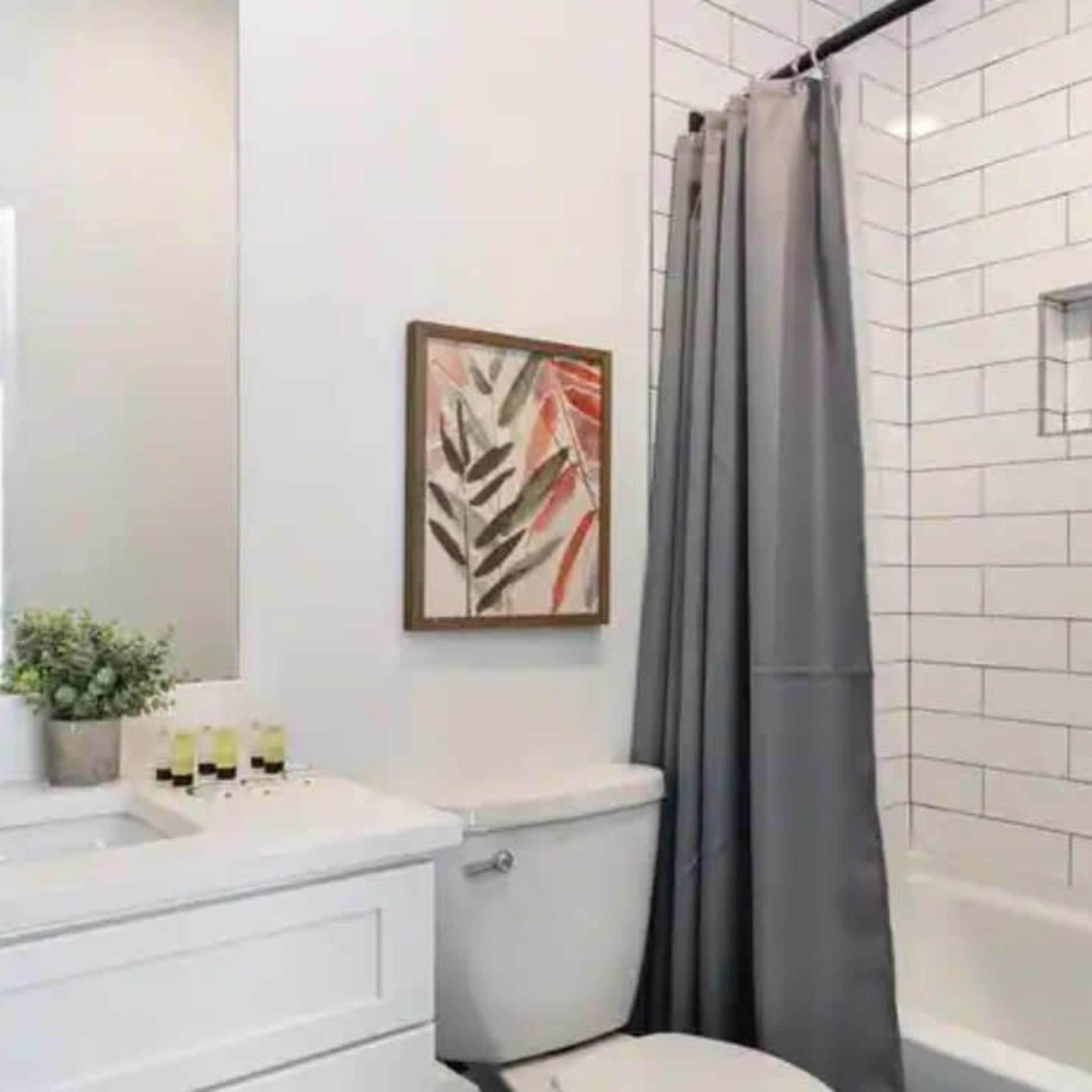A modern bathroom features a white subway tile shower, a gray curtain, a white vanity with a sink, and a framed botanical print on the wall.