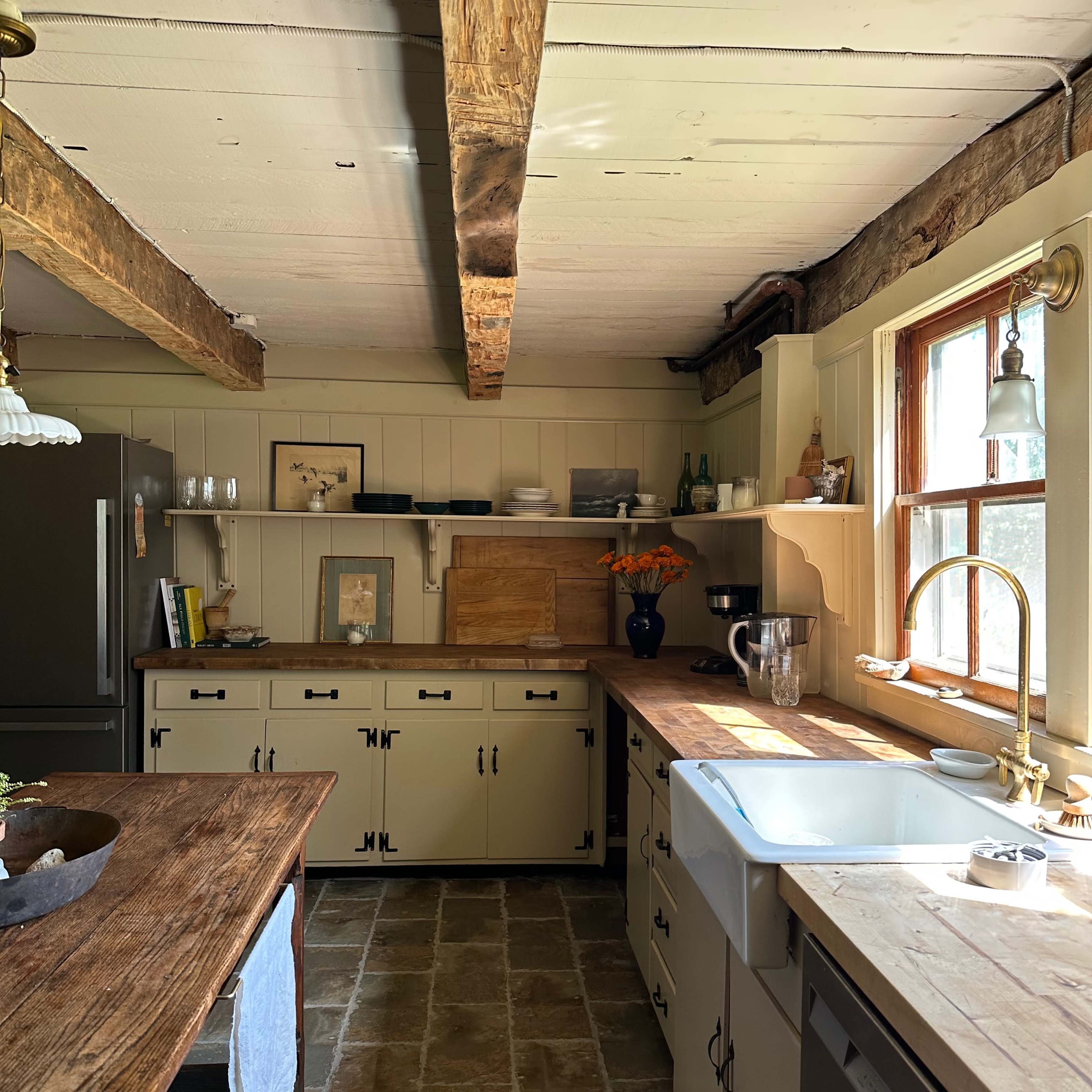 The kitchen features wooden beams, a large sink, and a central island with cabinets and shelving along the walls.