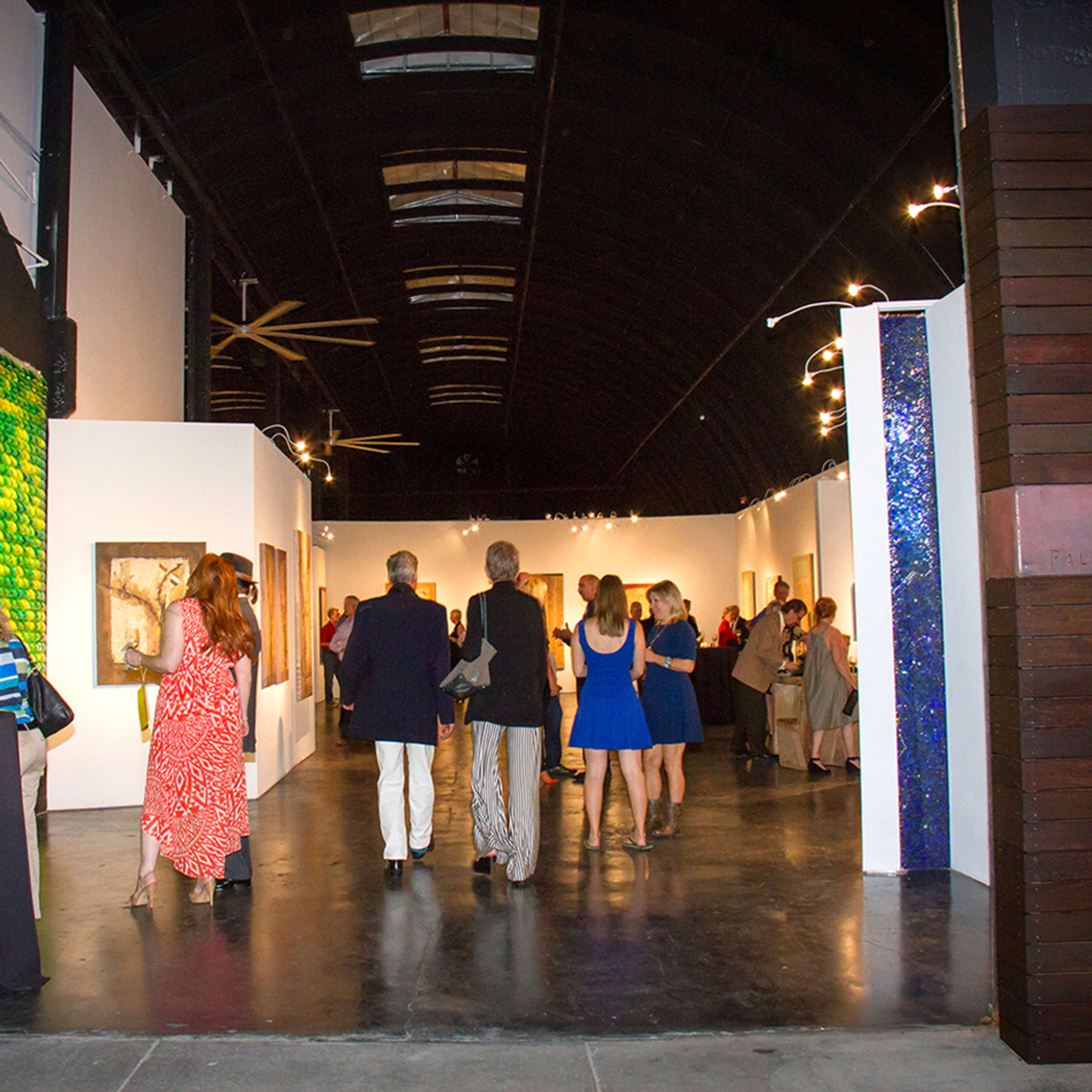 A group of people browse an art gallery featuring colorful paintings along the walls.
