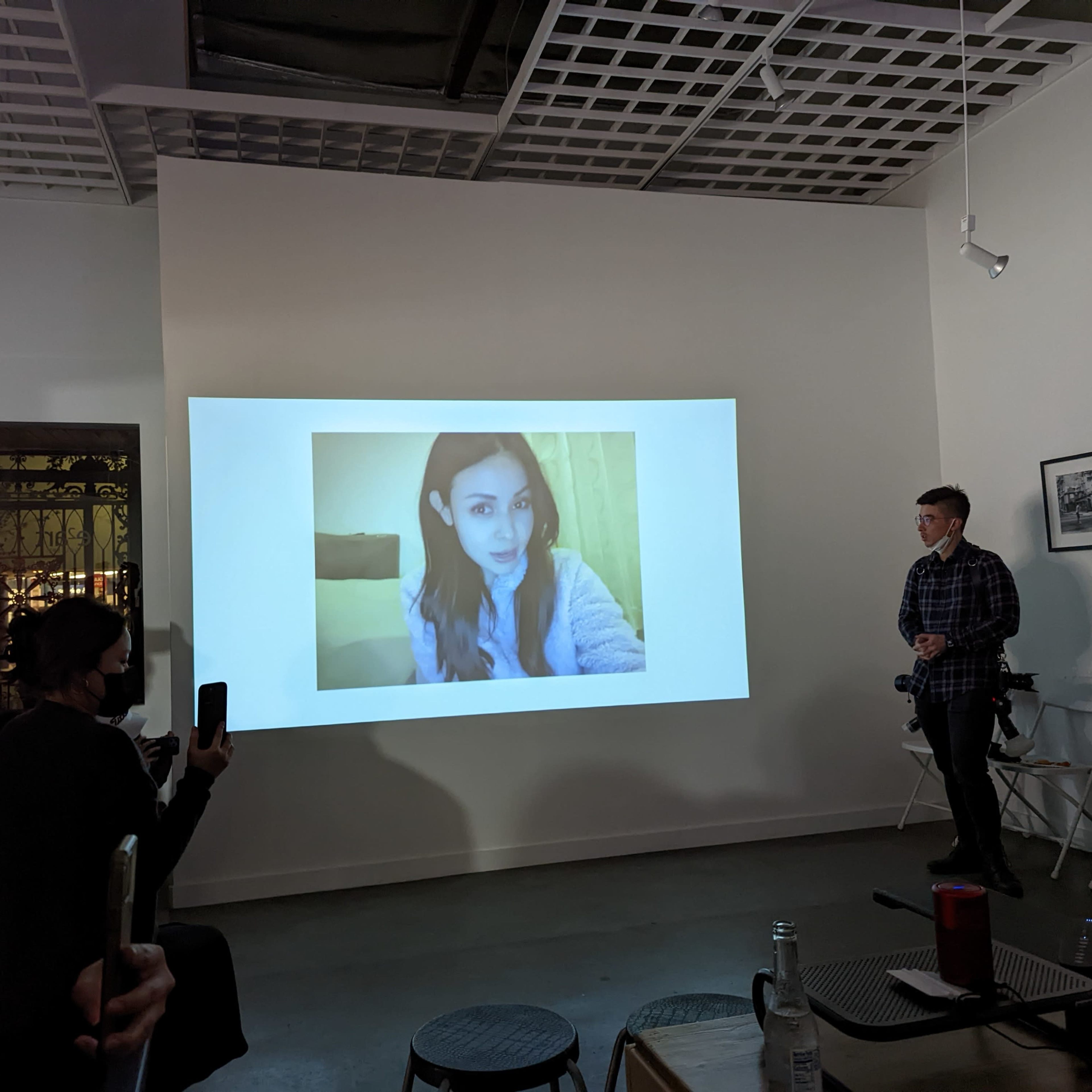 A group of people watches a presentation featuring a large photo on a white wall.