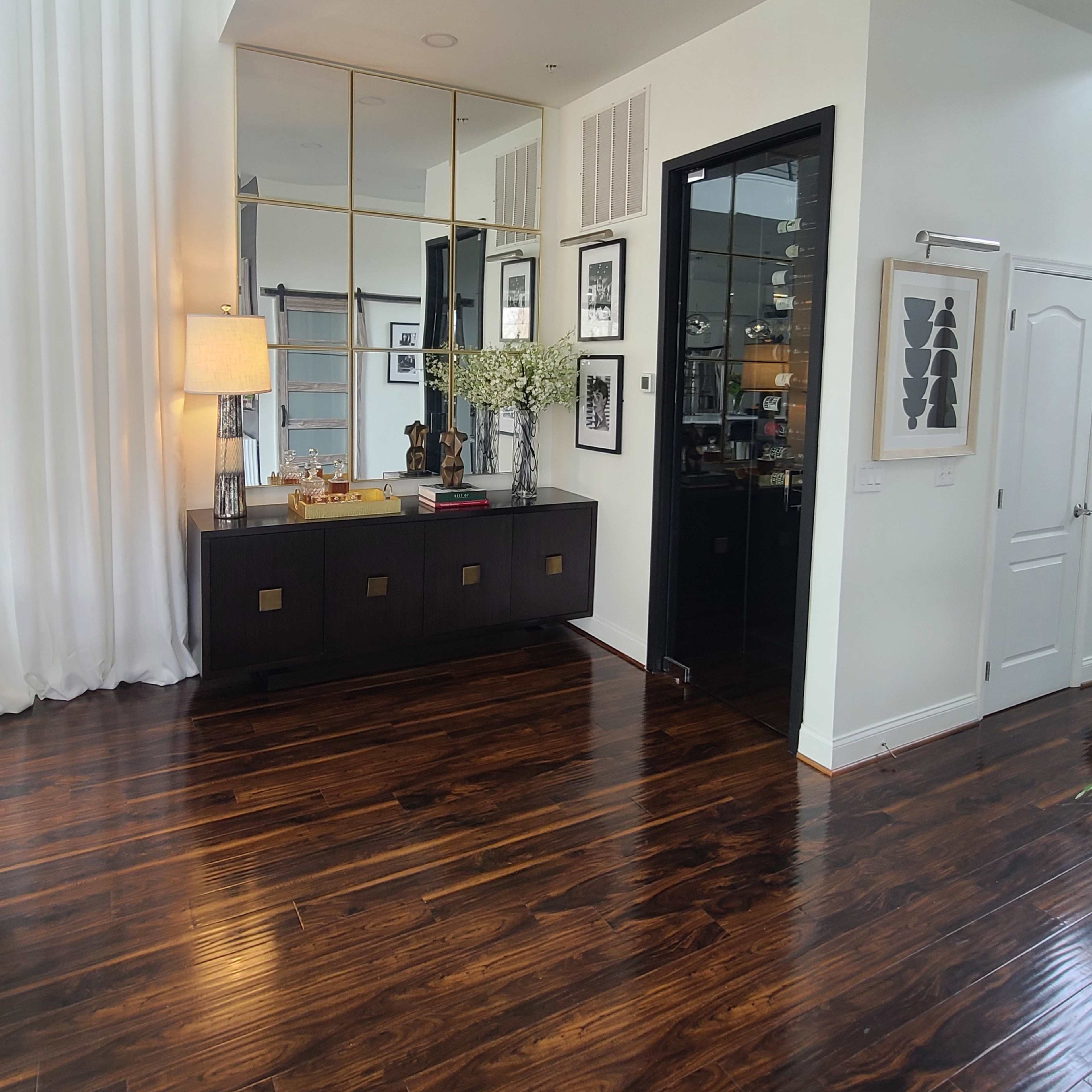 A modern entryway with dark wooden flooring, a console table adorned with decorative items, and a large mirror reflecting a light-filled space.
