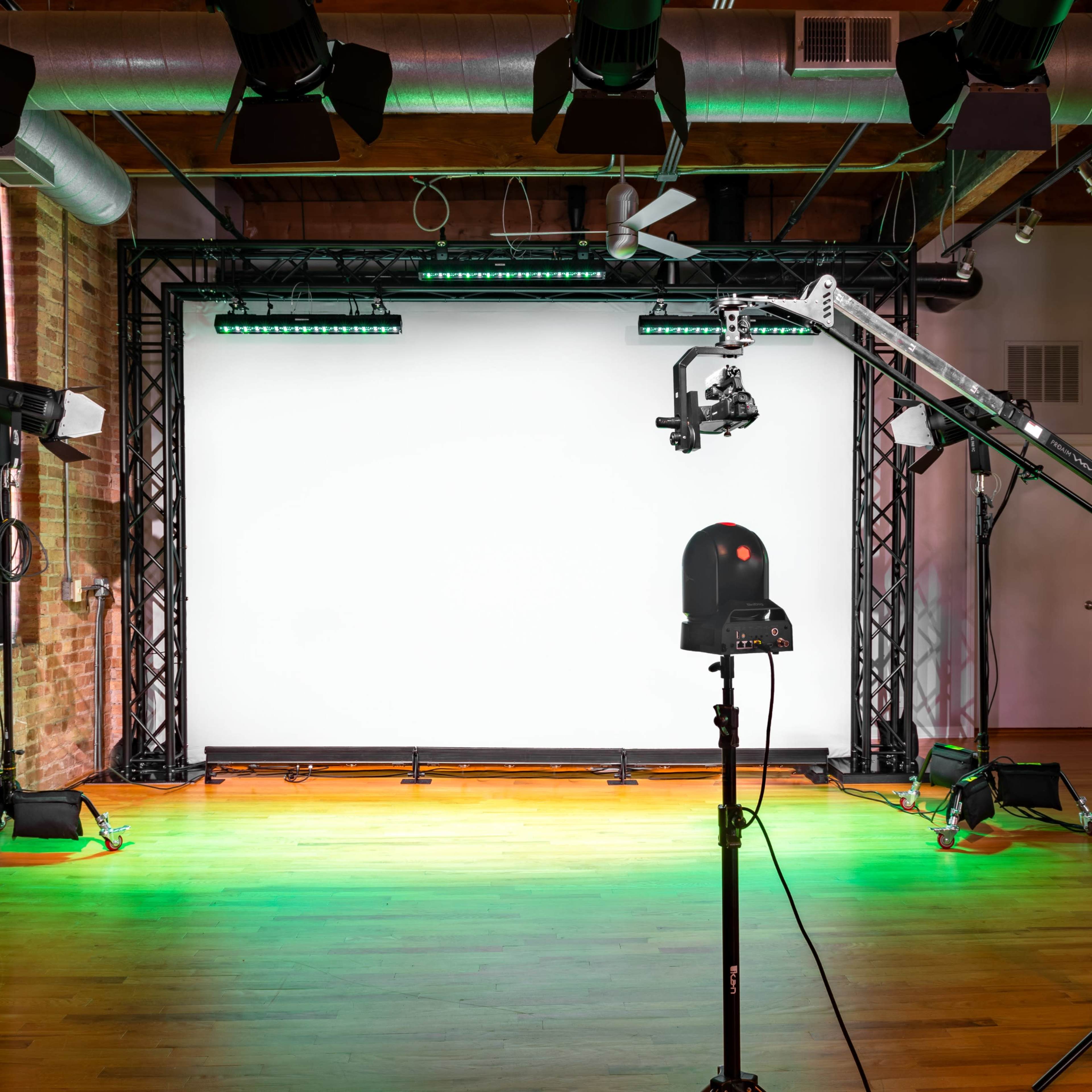 A photography studio setup with a blank white backdrop, lighting equipment, and a camera crane on a wooden floor.