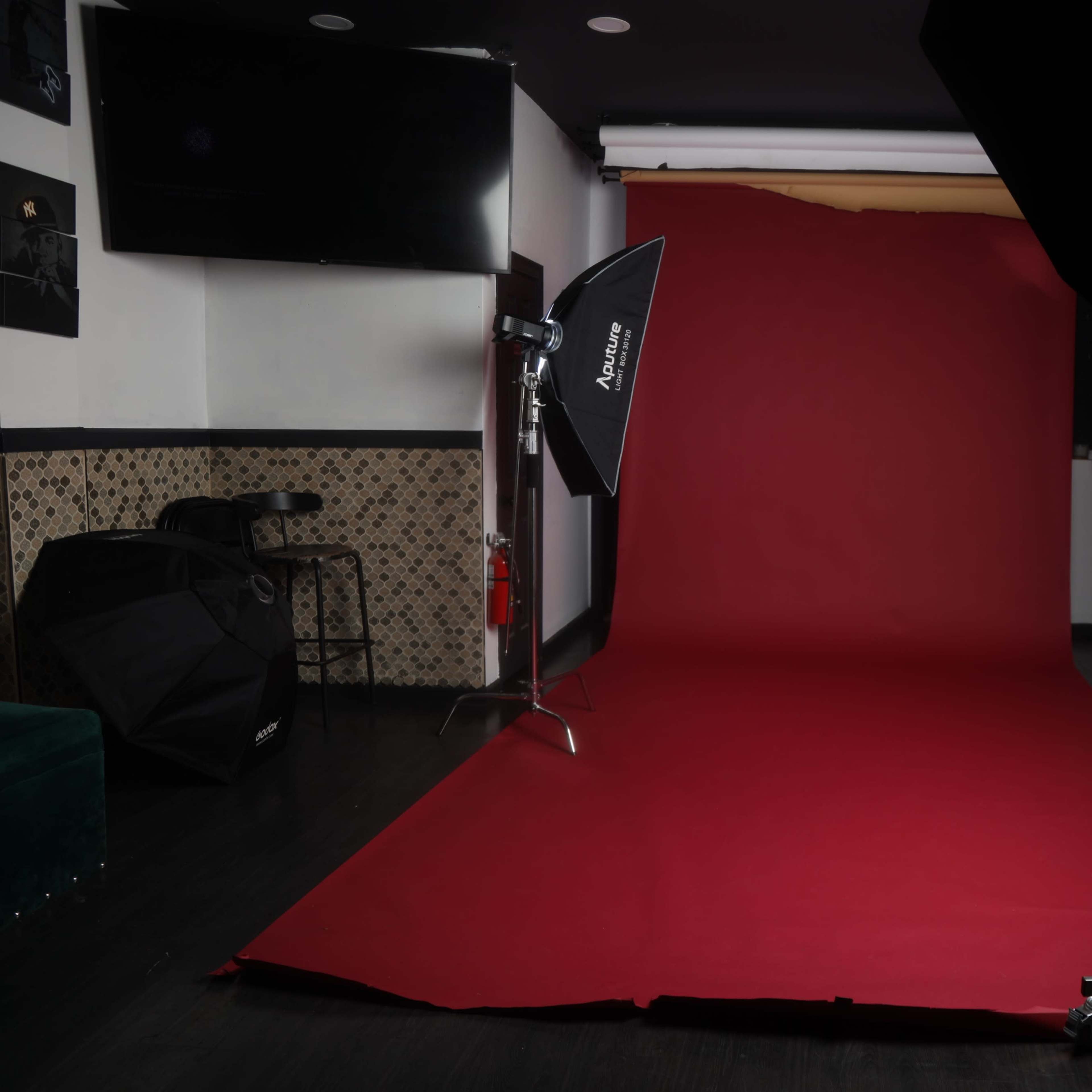 A photography studio setup featuring a red backdrop, softbox lights, and a dark wooden floor.