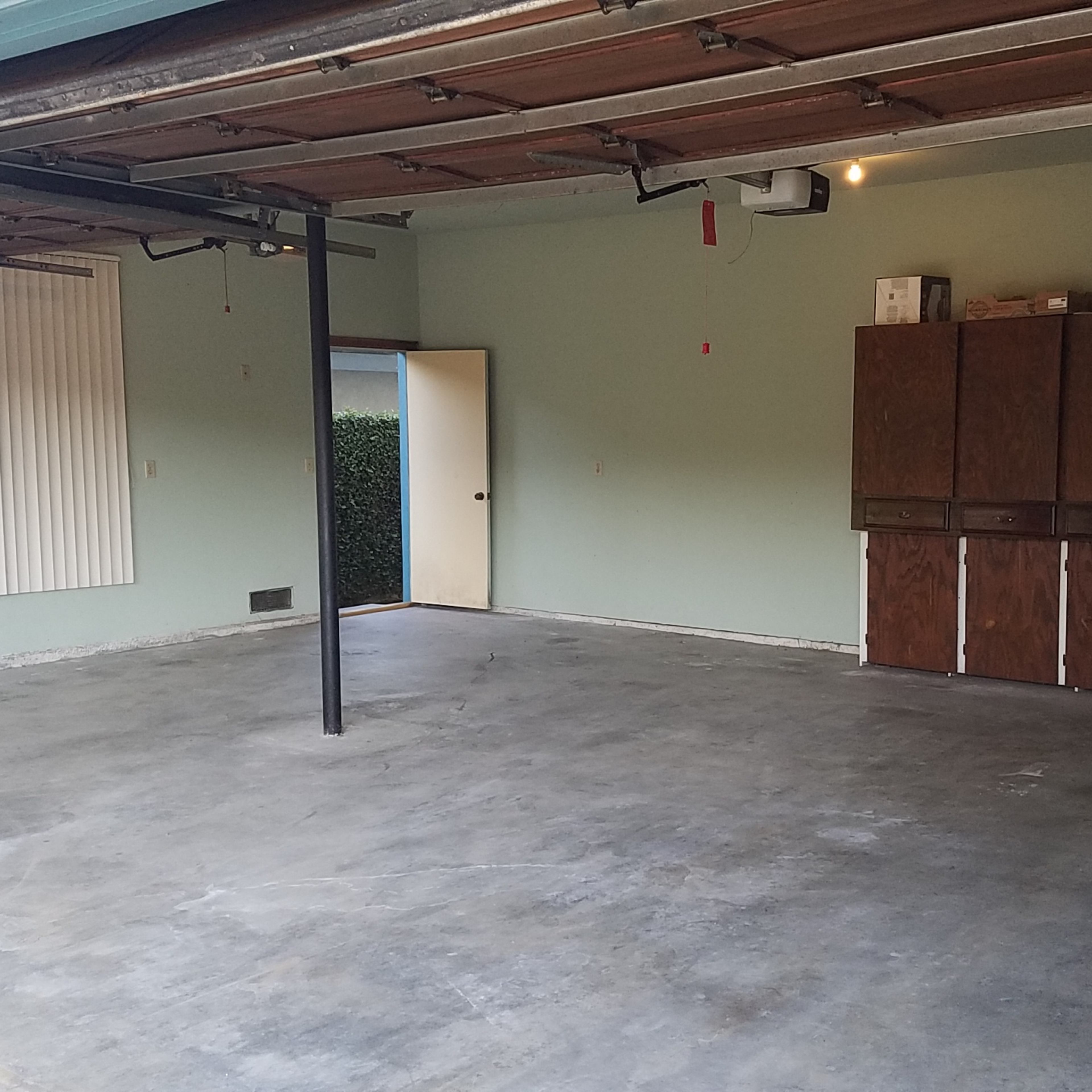 An empty garage with a concrete floor, green walls, and overhead storage cabinets along one side.