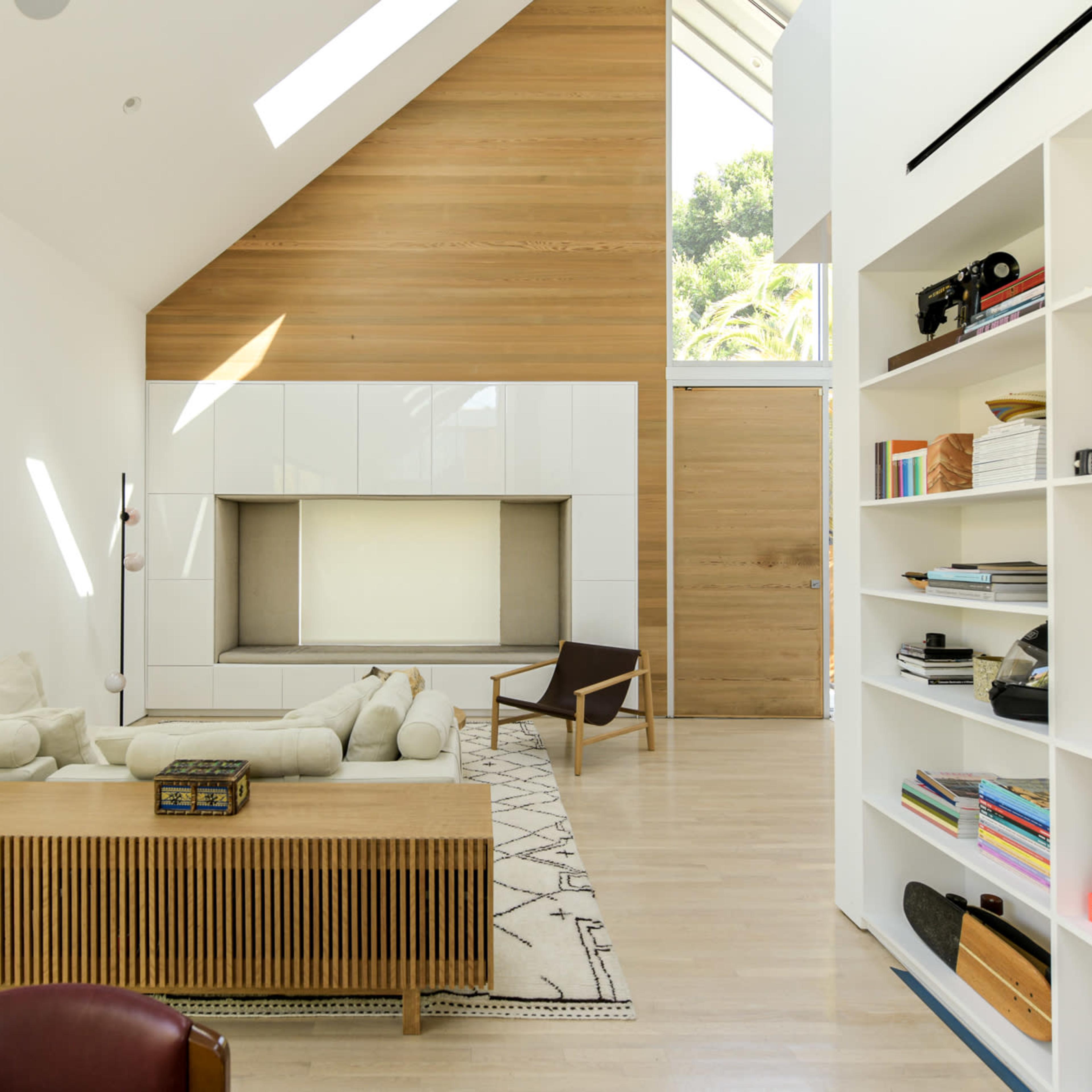 A spacious living room features a large white sectional sofa, a wooden coffee table, and shelves filled with books and decorative items.