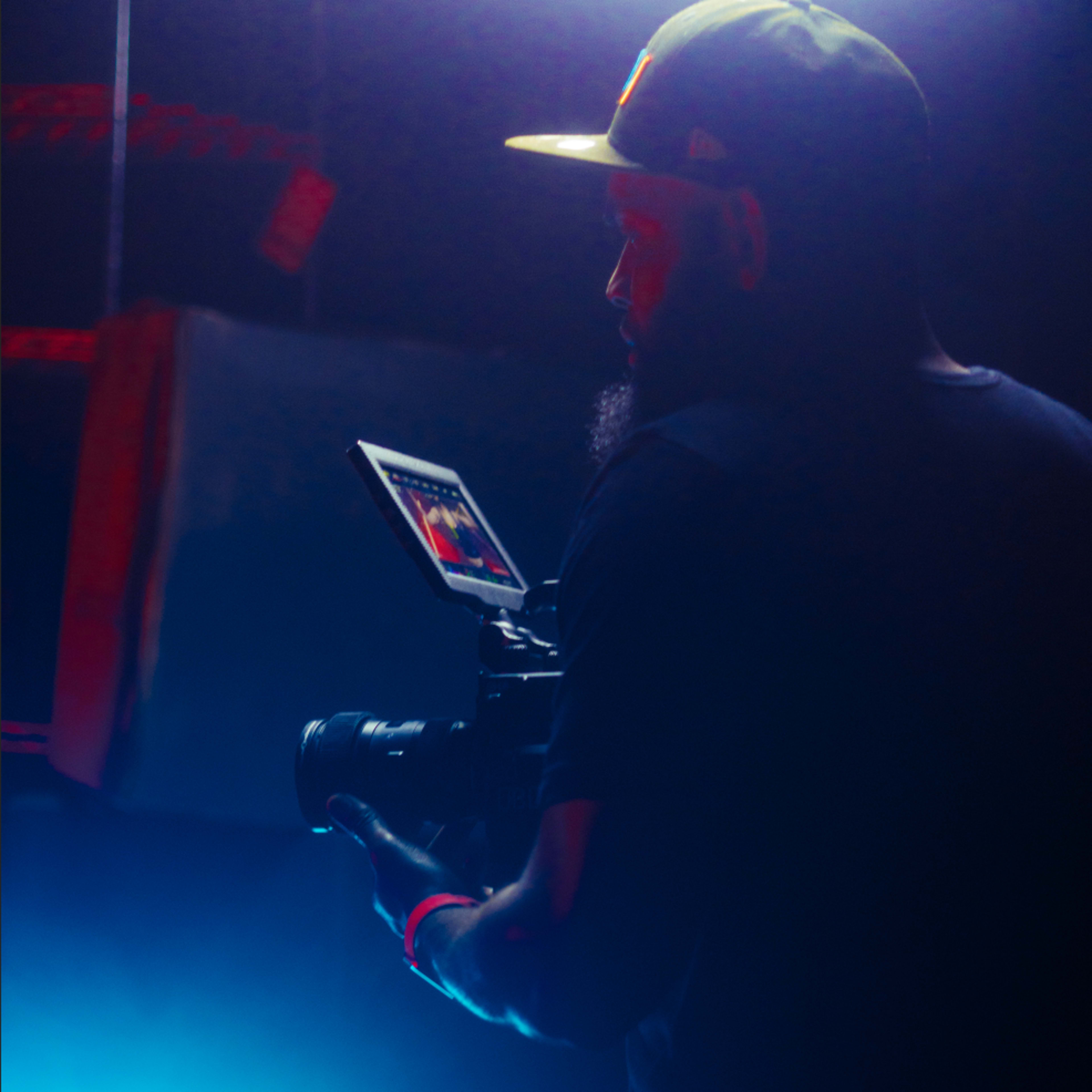 A person with a camera is filming in a dimly lit environment illuminated by blue and red lights.