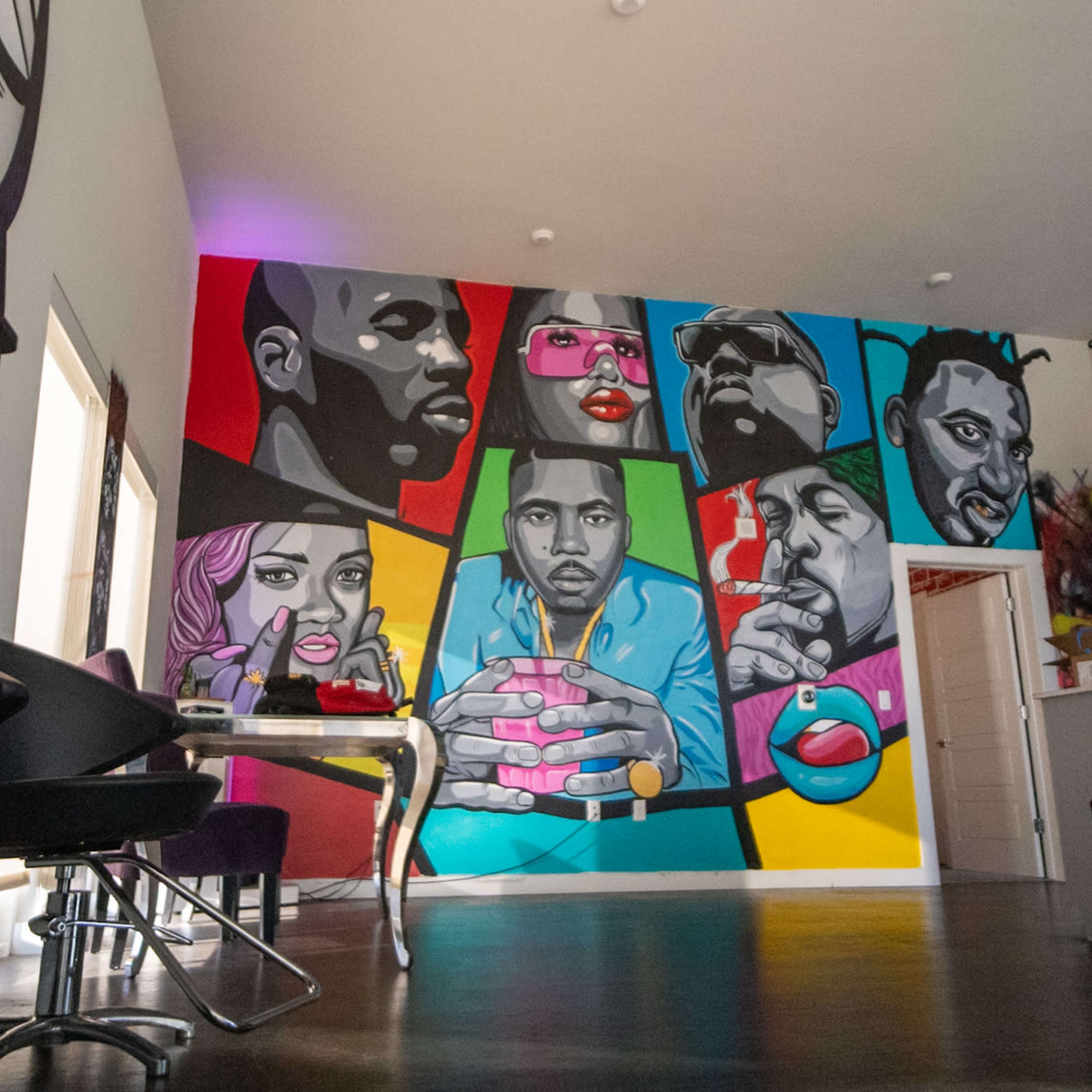 A colorful mural on a wall featuring portraits of various individuals in a modern interior space with a kitchen area visible.