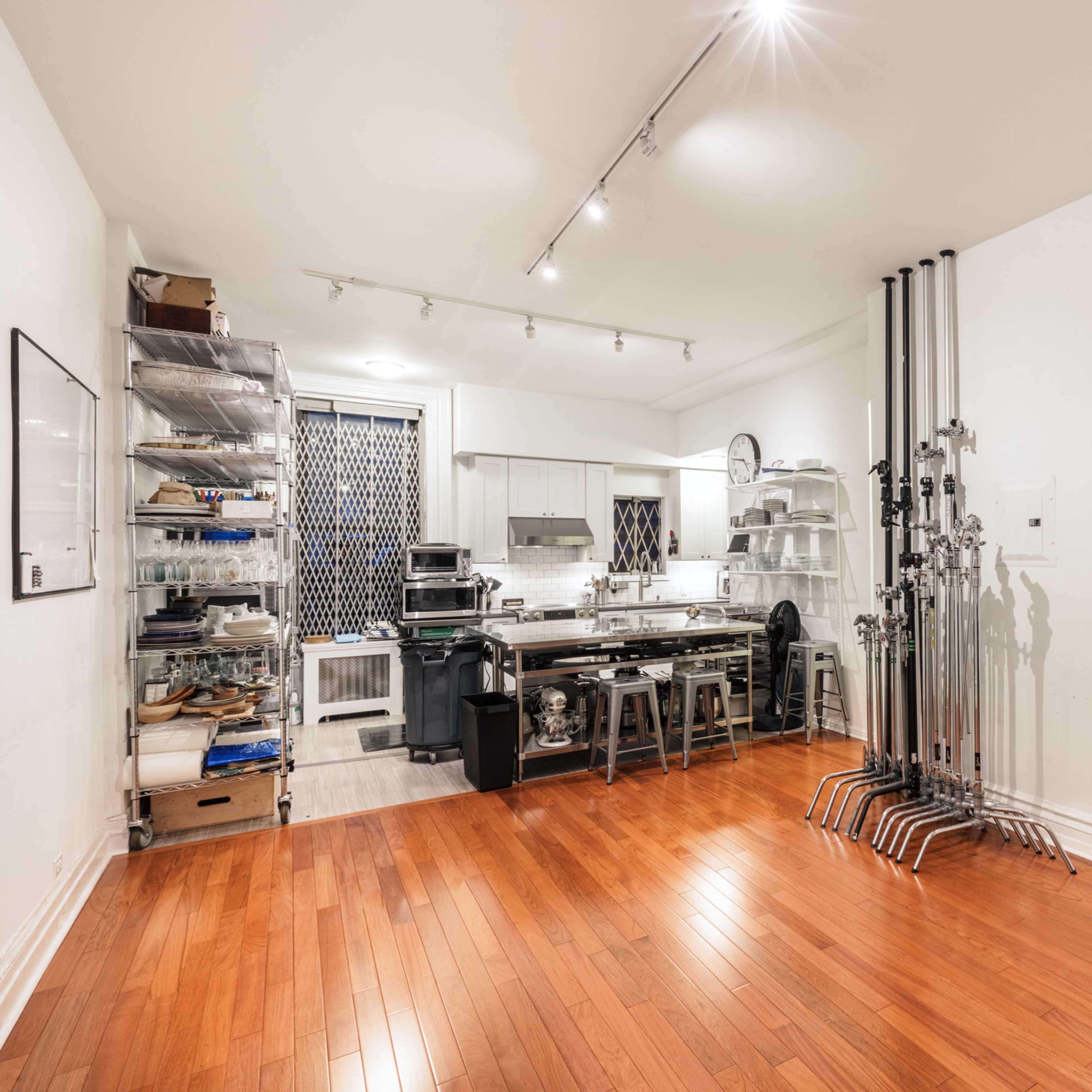 A modern kitchen with stainless steel appliances, a wooden floor, and various kitchen items organized on metal shelves.