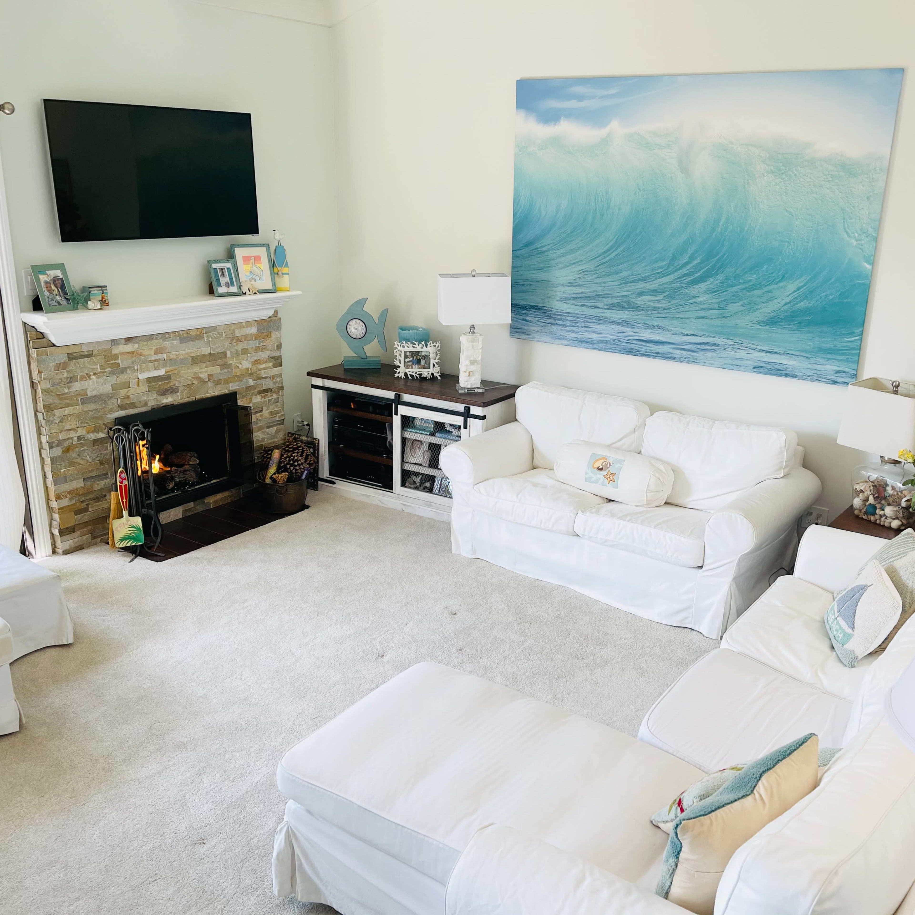 The living room features white furniture, a stone fireplace, and a large wave painting above the mantel.