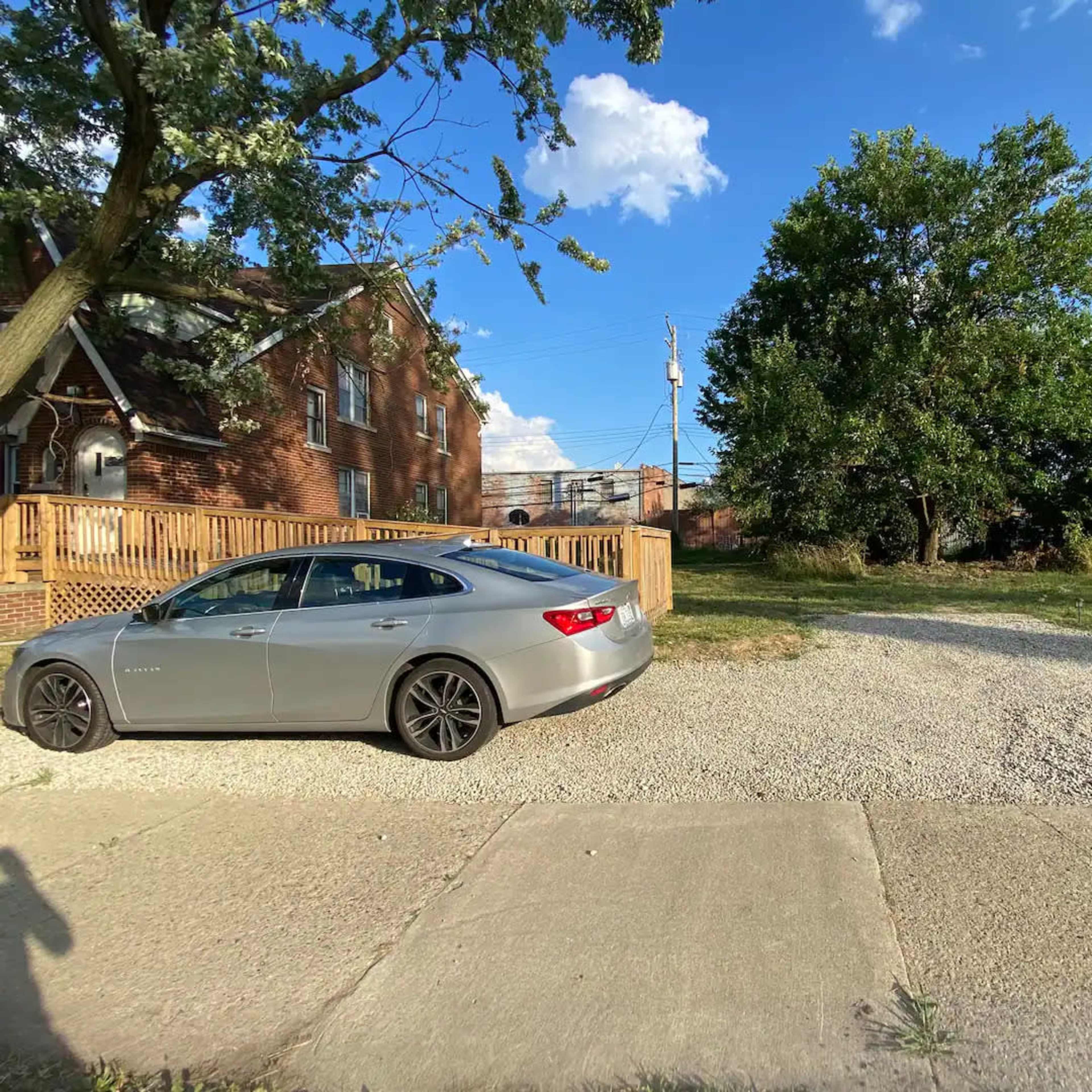 A silver car is parked on a gravel driveway beside a grassy area and a two-story brick building.