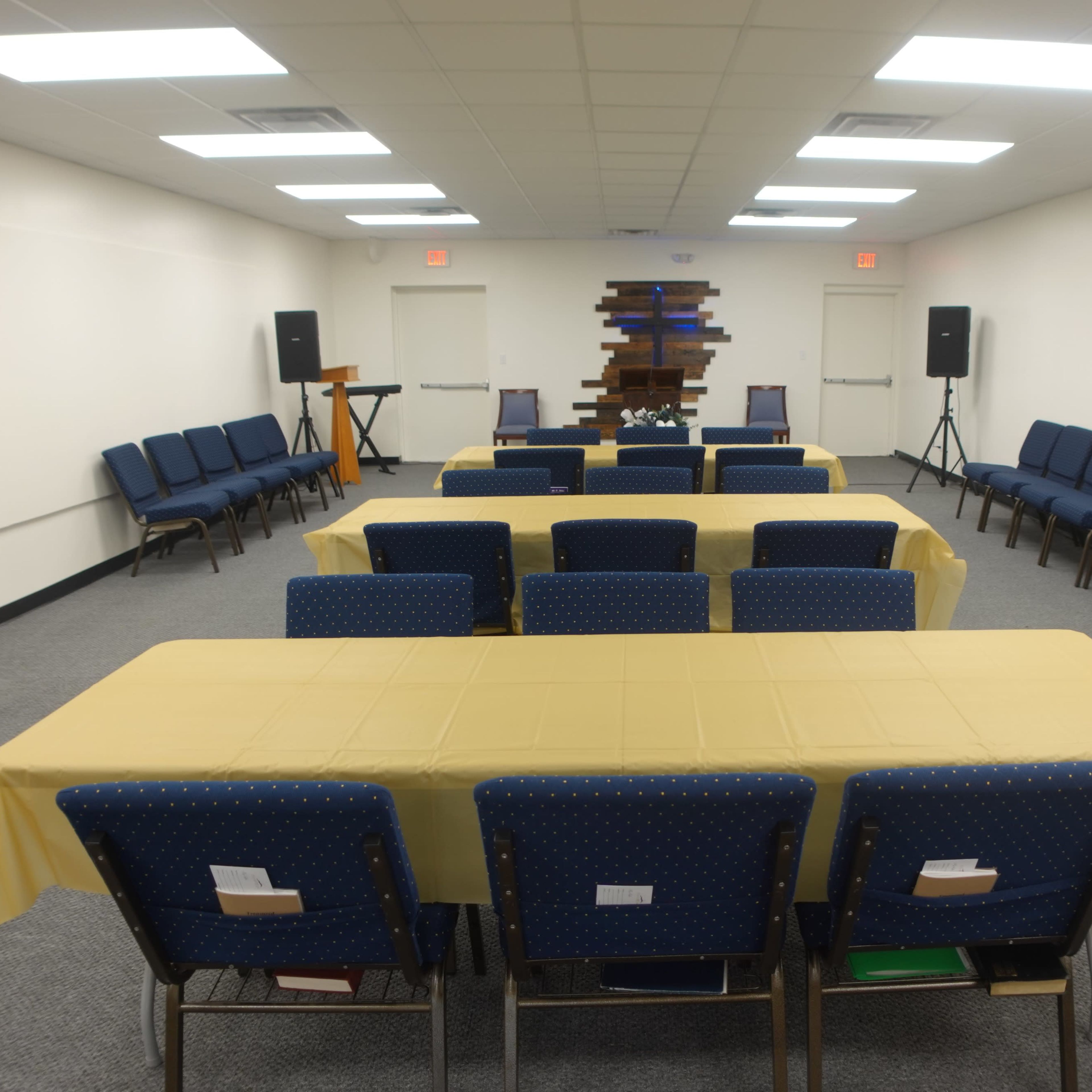 A meeting room is set up with two rows of blue chairs and several tables covered with yellow tablecloths.