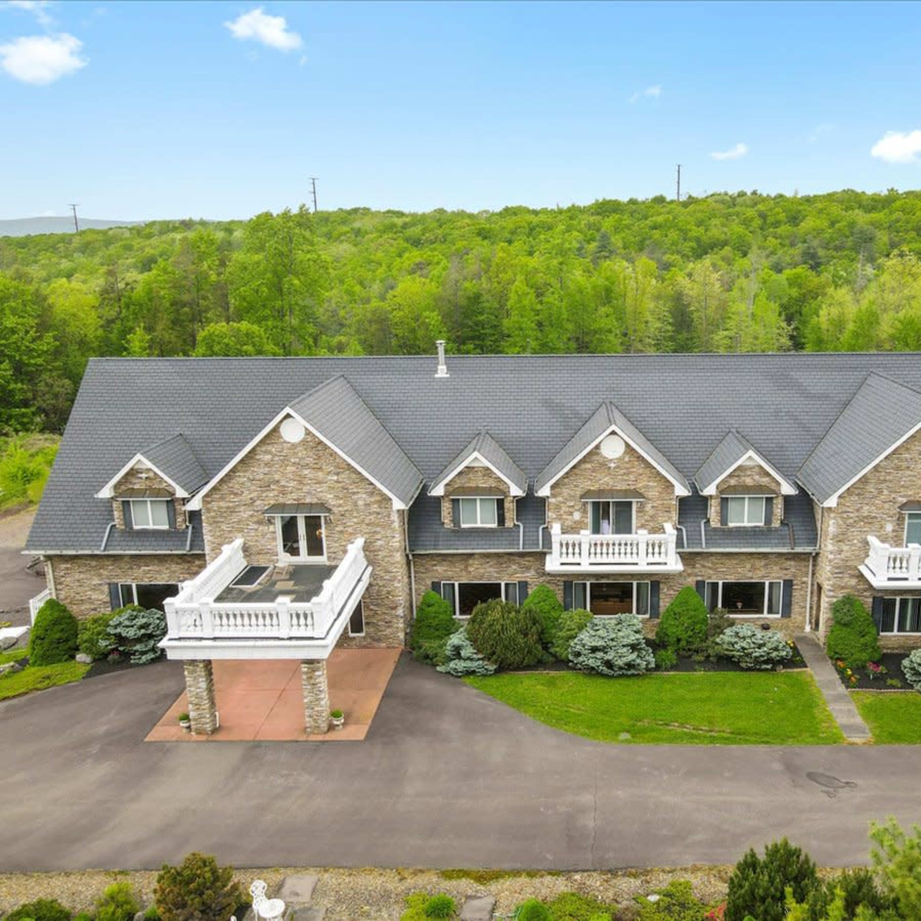 A large, stone-faced building with multiple sections and balconies, surrounded by landscaped greenery and a paved driveway.