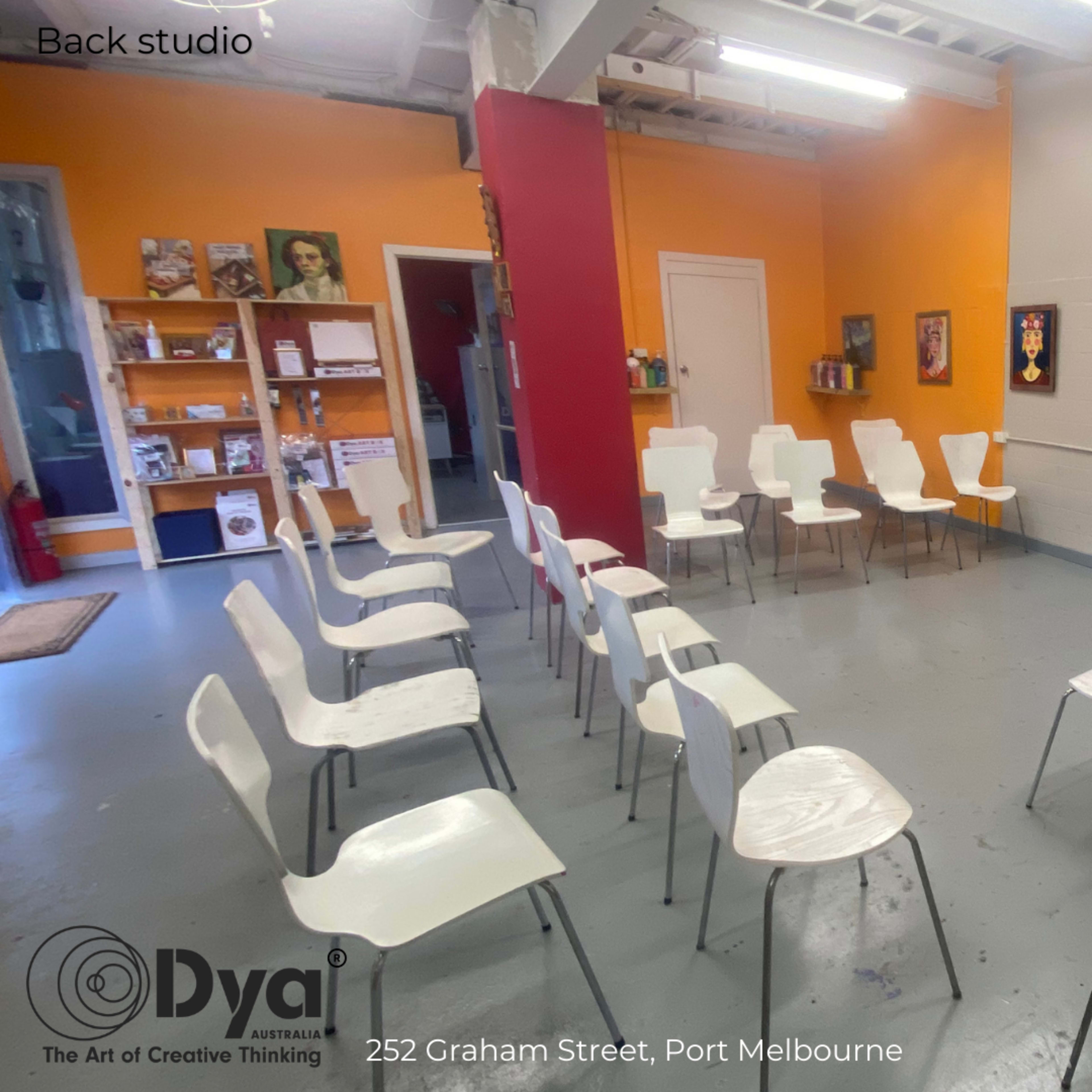A studio space in Port Melbourne with white chairs arranged in a circular formation, surrounded by orange and white walls featuring artwork and inspirational phrases.