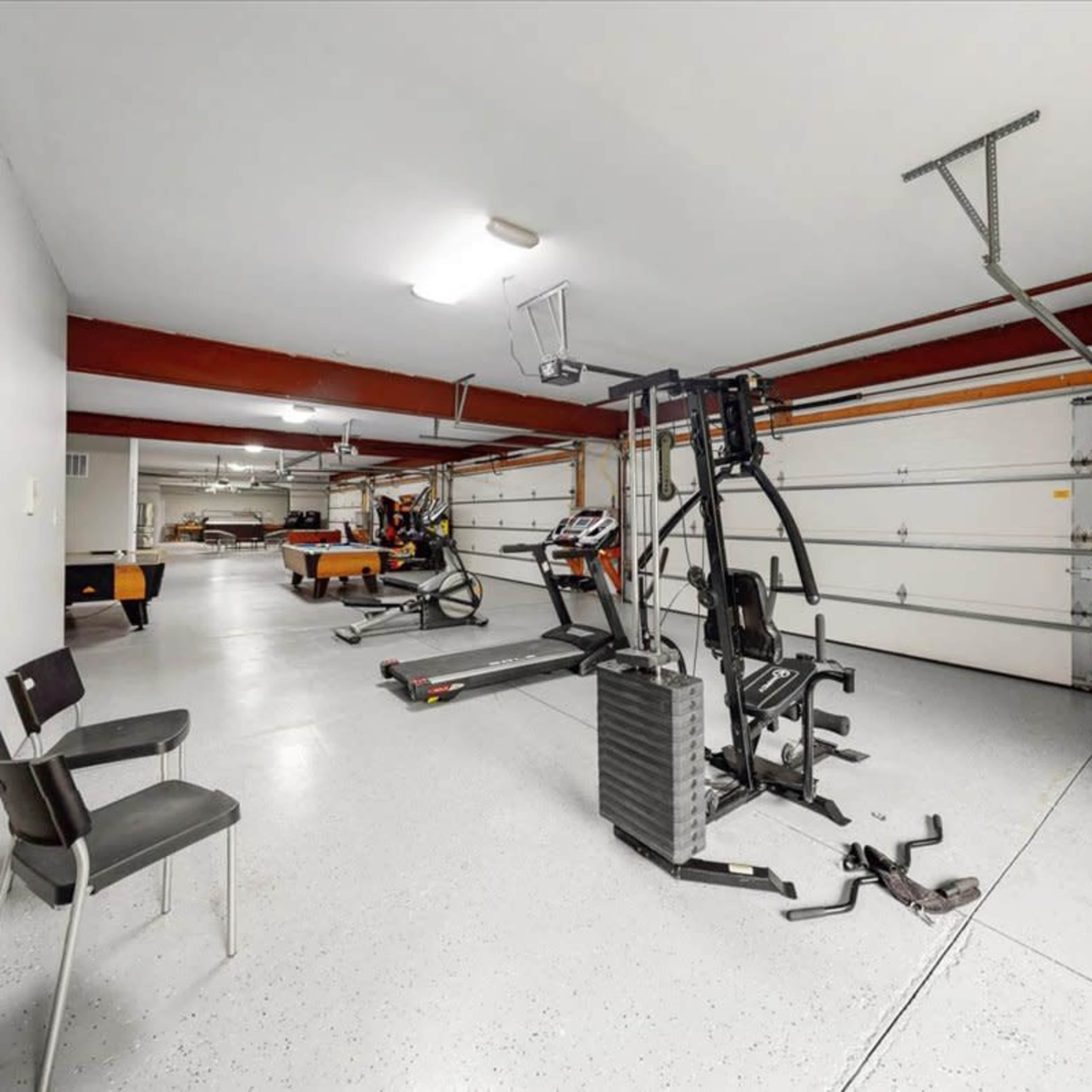 A spacious garage equipped with exercise equipment and a chair, along with multiple garage doors in the background.