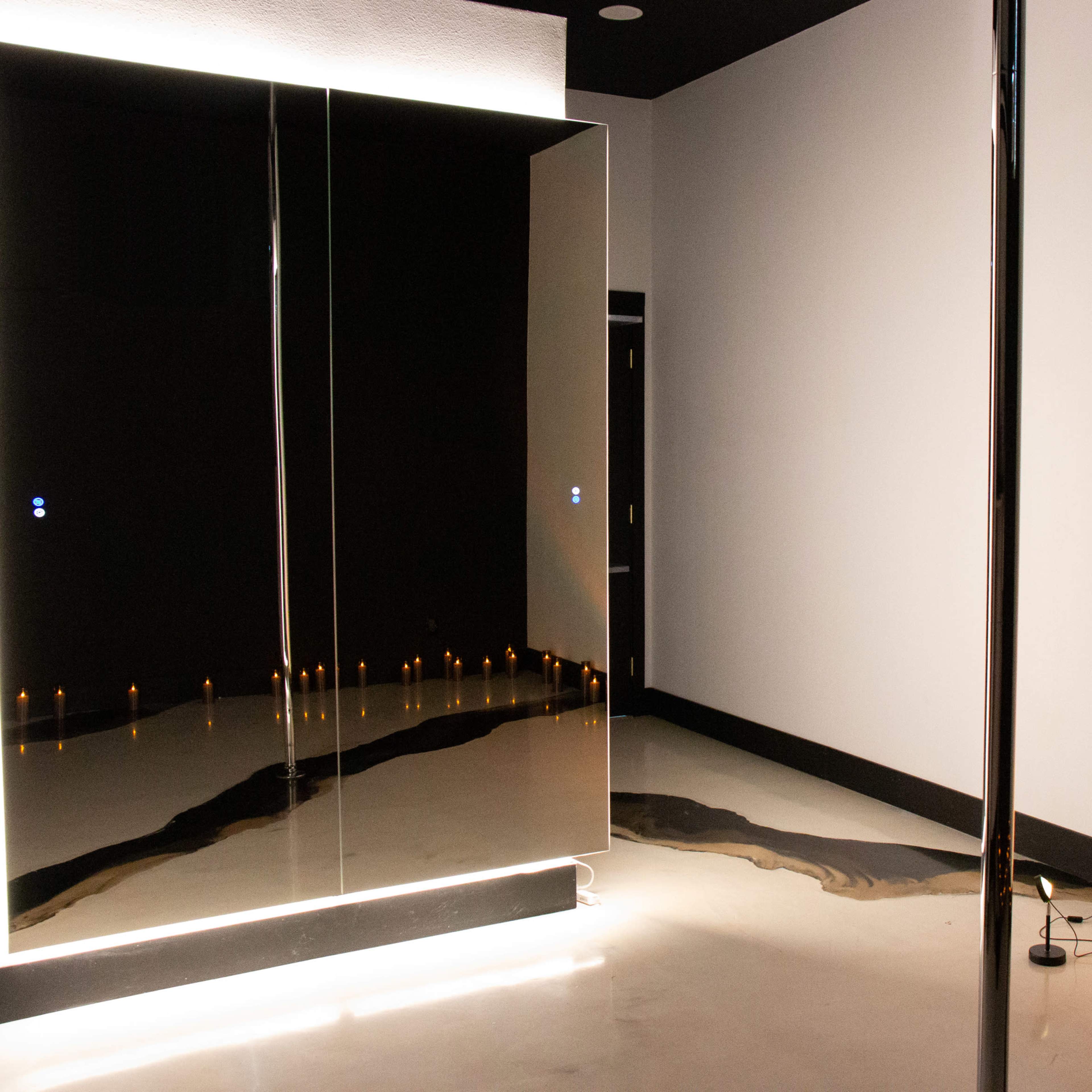 A dimly lit room with a large mirror and a polished floor, featuring a line of candles along one side.