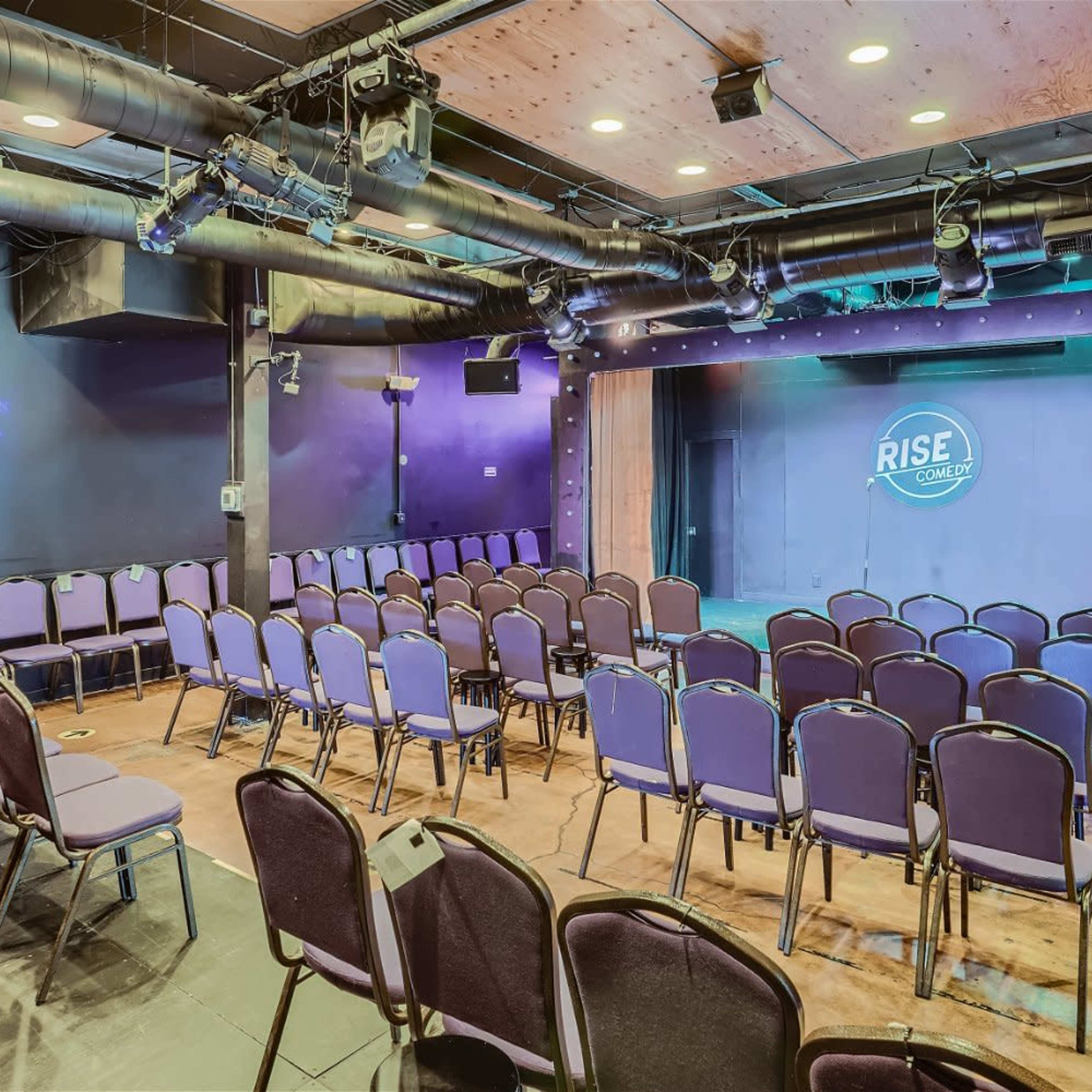 A small performance venue with rows of purple chairs facing a stage, featuring a logo that says "RISE."