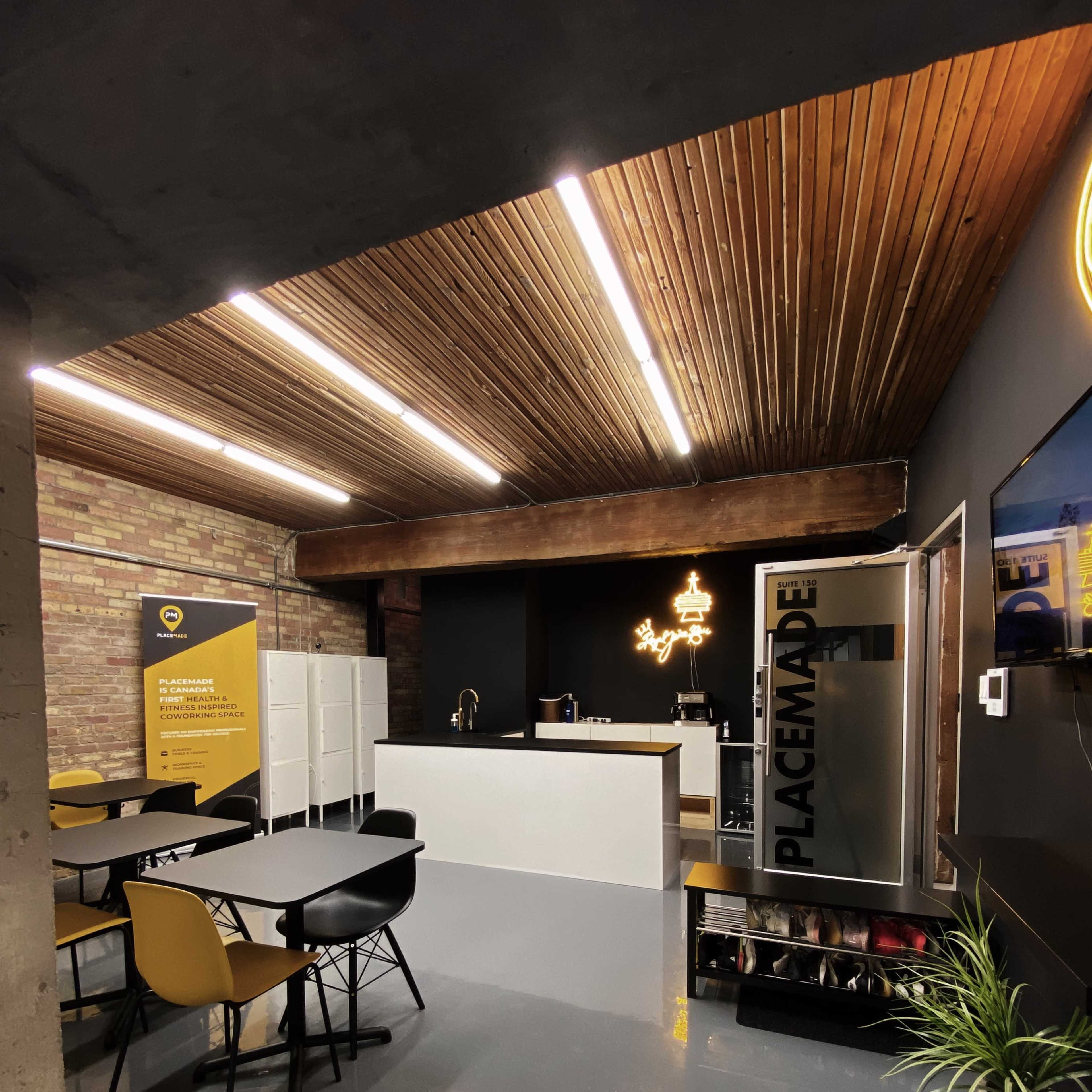 A modern indoor workspace featuring a wooden ceiling, a reception area with a counter, and several black and yellow chairs arranged around tables.