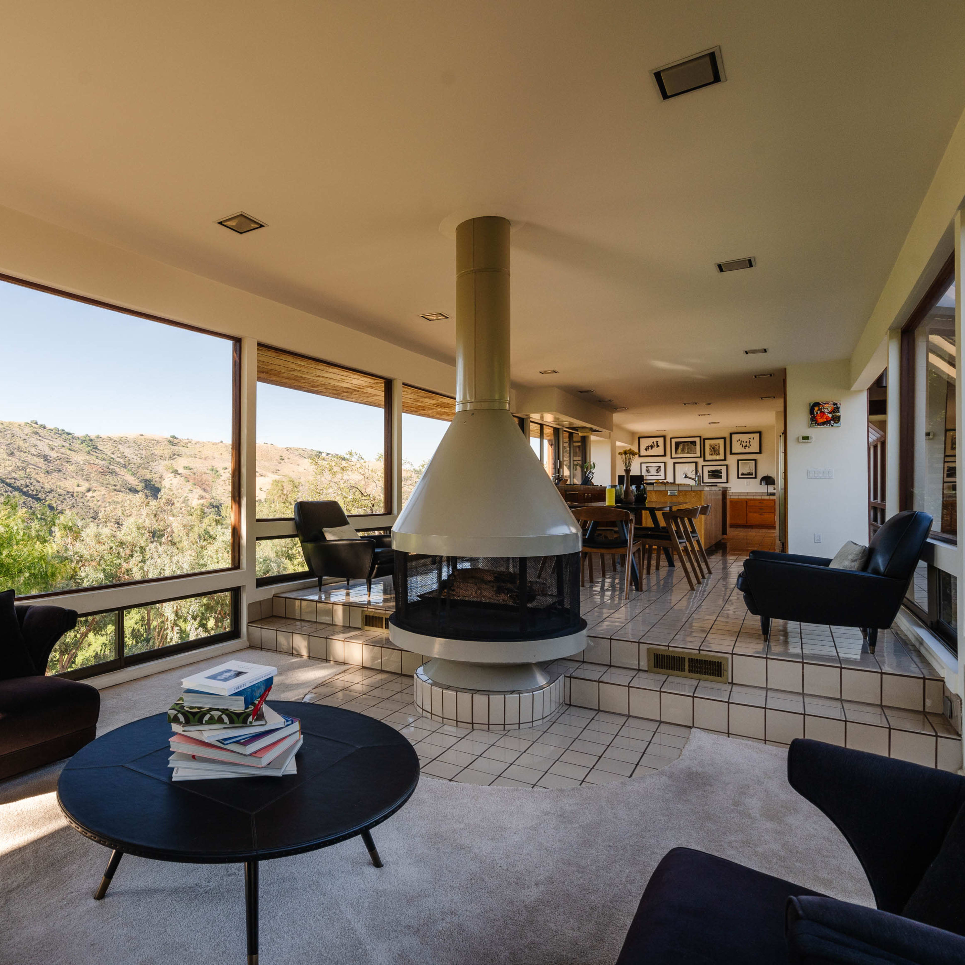A modern living room features a central fireplace and large windows that showcase a scenic view of the surrounding landscape.