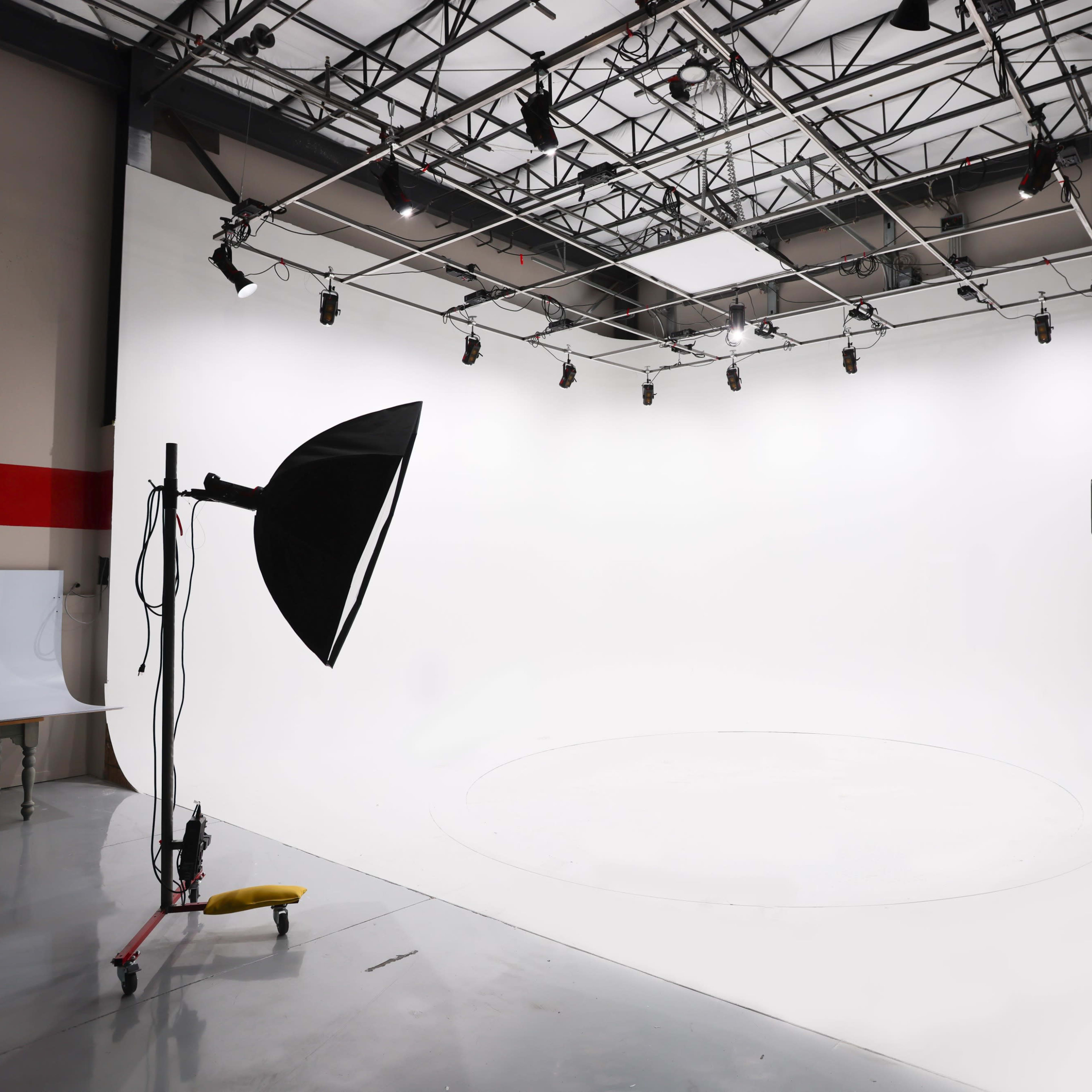 A photo studio with a seamless white backdrop, equipped with two large softbox lights positioned on either side.