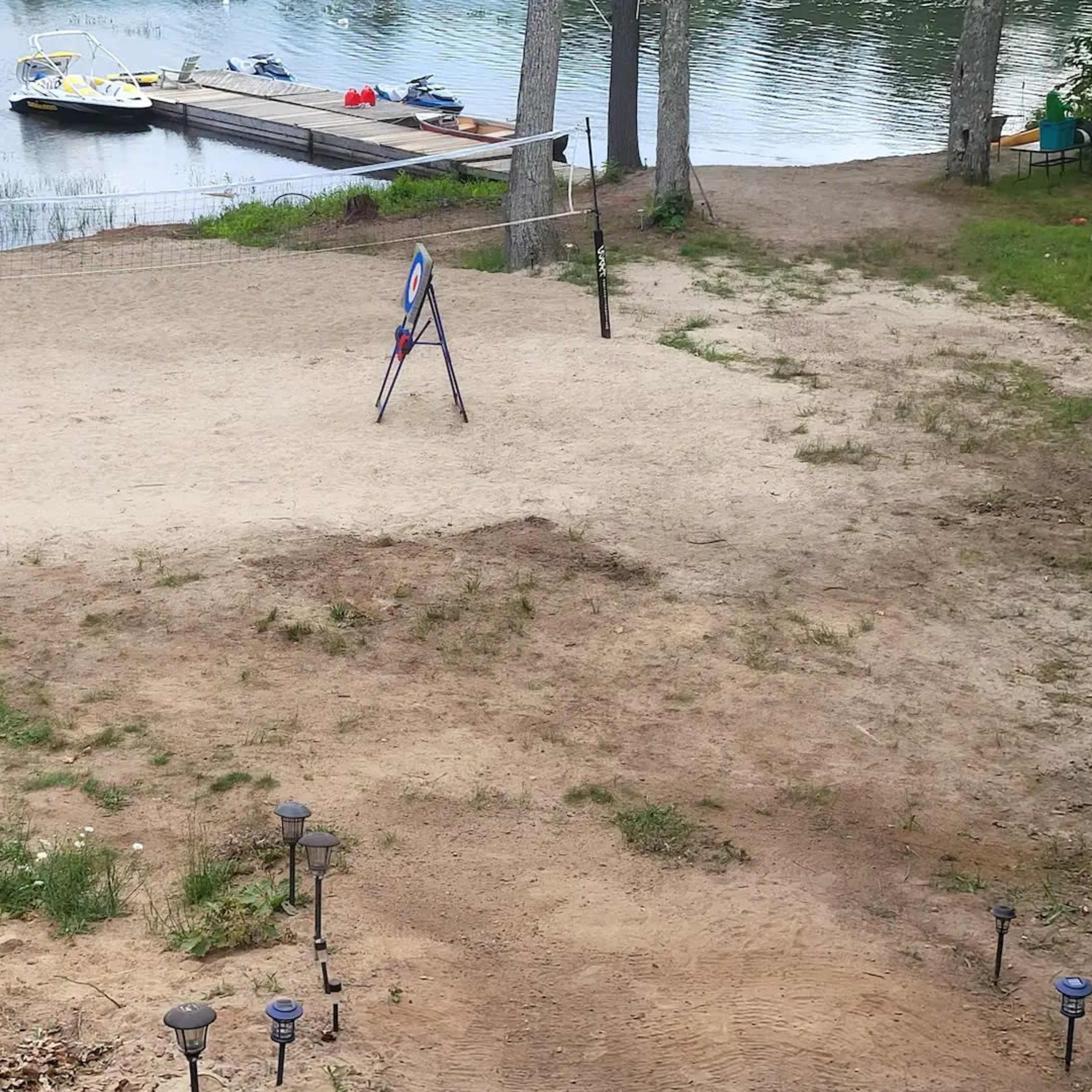 A sandy area near a calm body of water, with a dock and parked personal watercraft in the background.