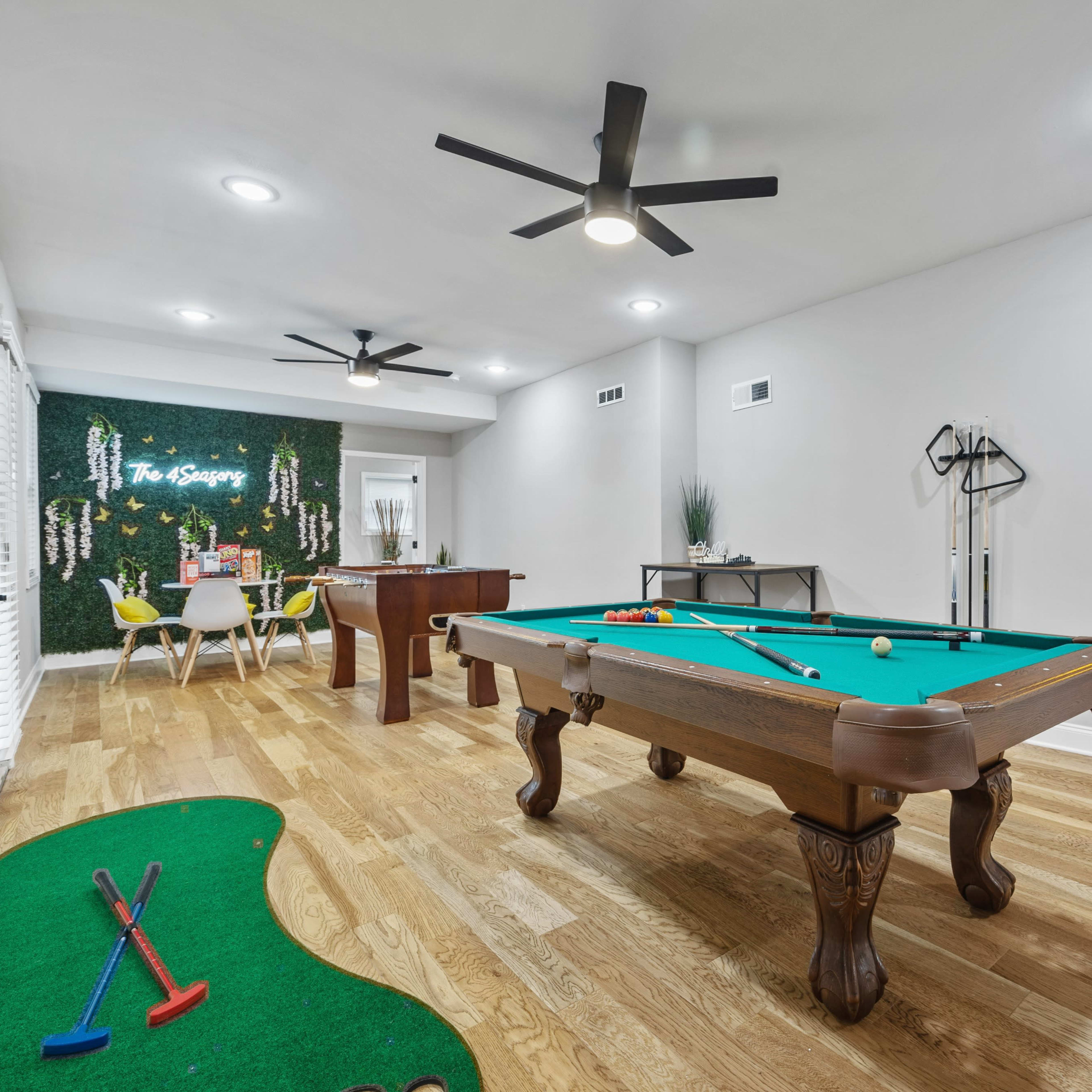A game room featuring a pool table, a putting green, and a seating area with a wall covered in greenery.