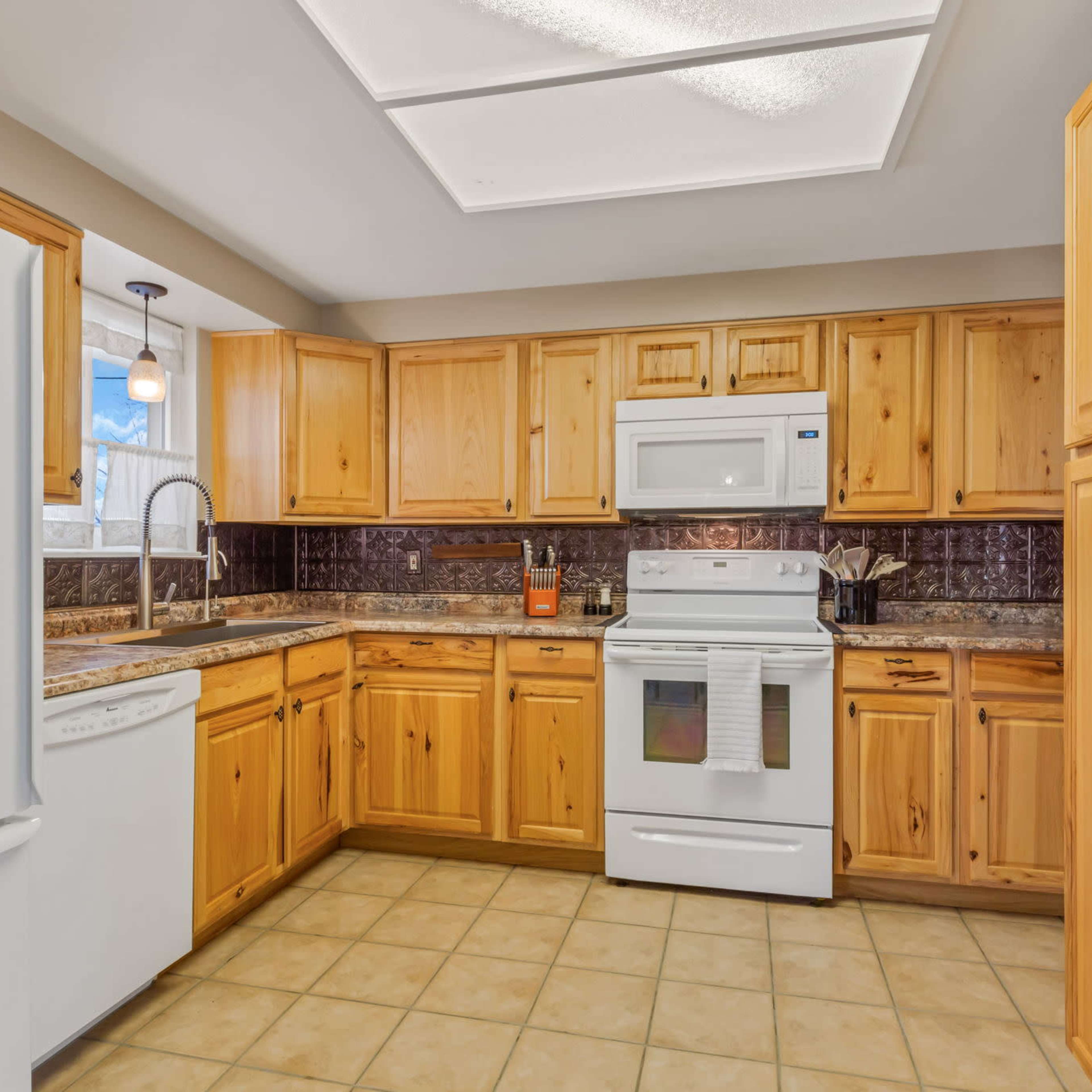 A kitchen features wooden cabinetry, white appliances, and a tile floor.