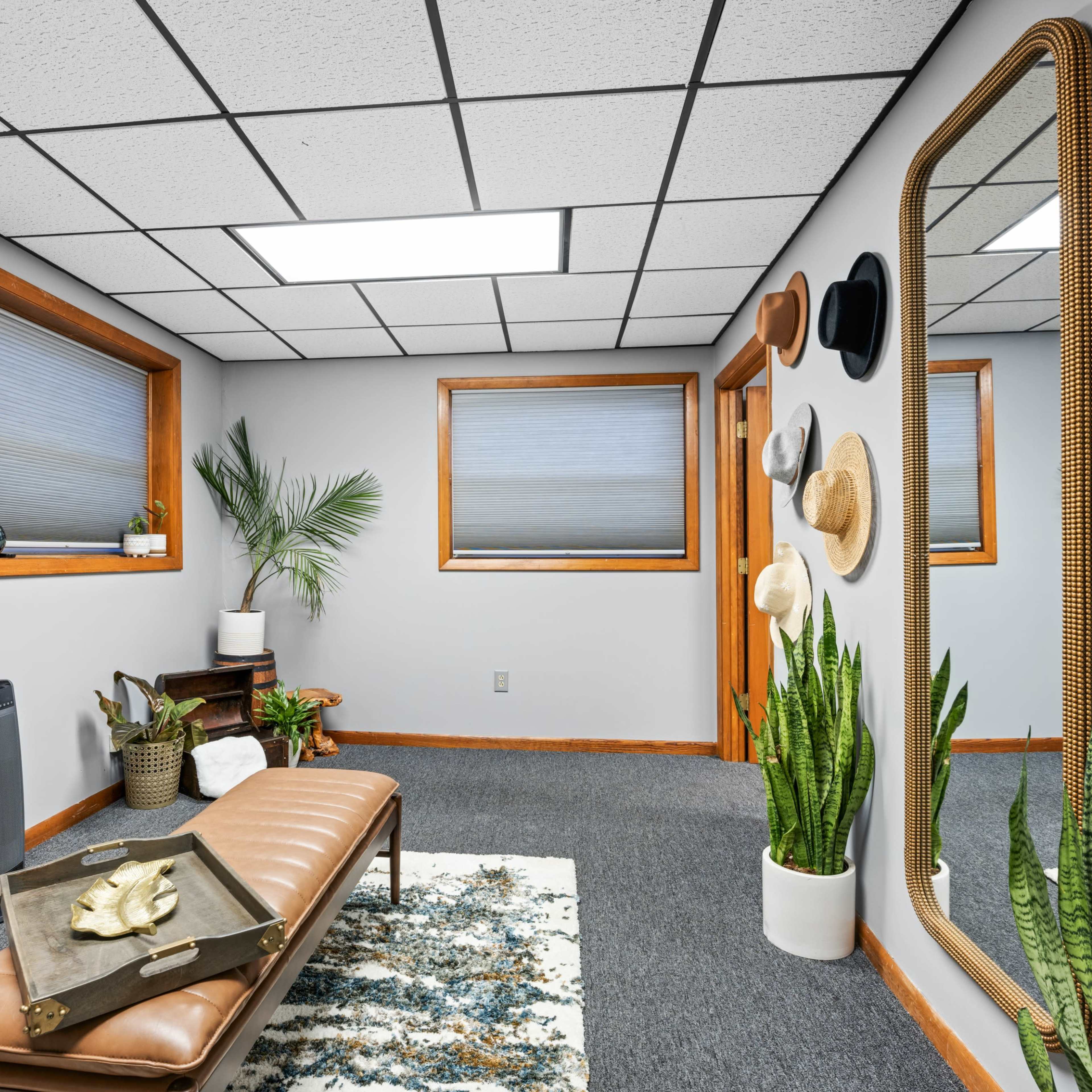 A bright room featuring a bench, potted plants, a large mirror, and hats displayed on the walls.