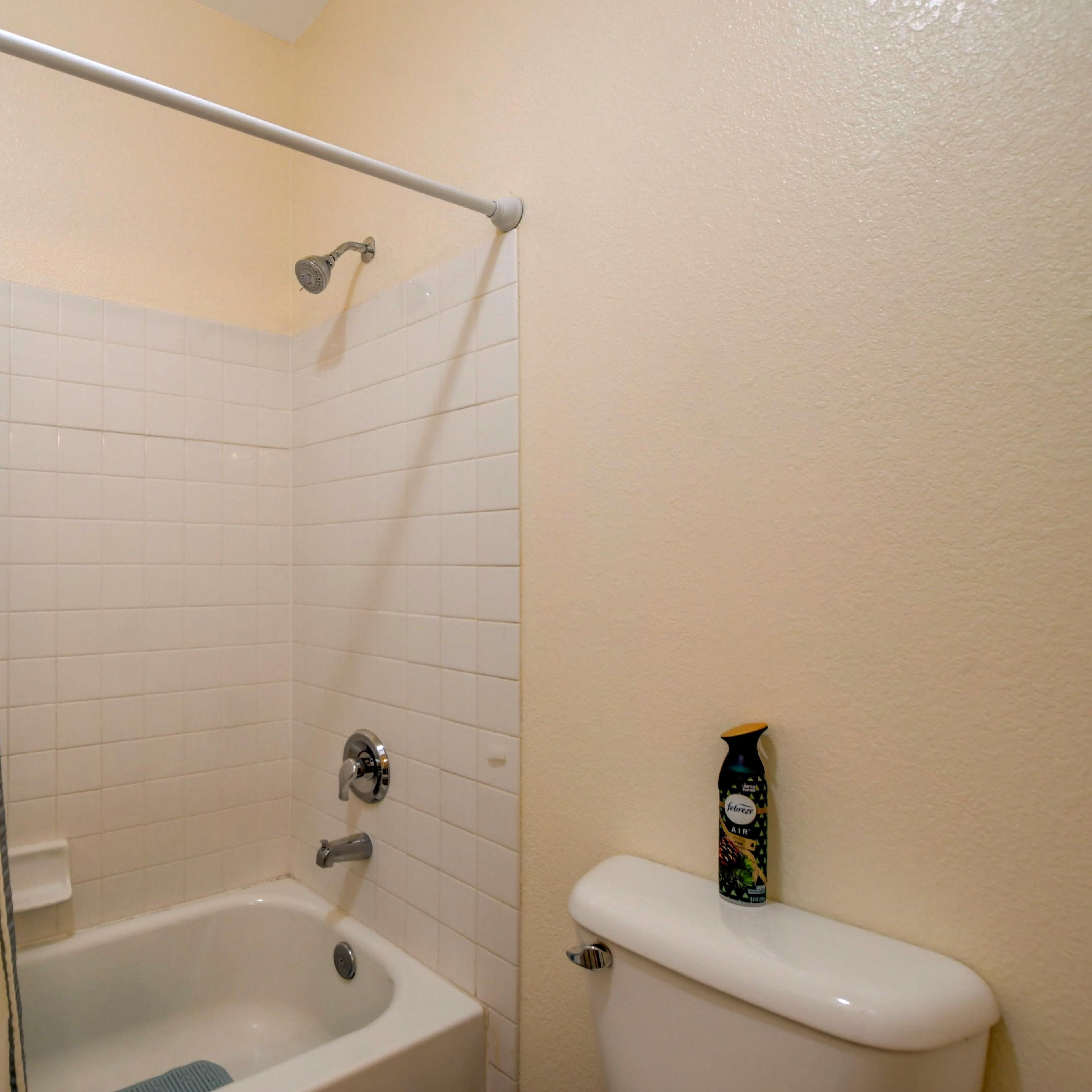 A bathroom with a shower, a bathtub, a toilet, and white tiled walls.