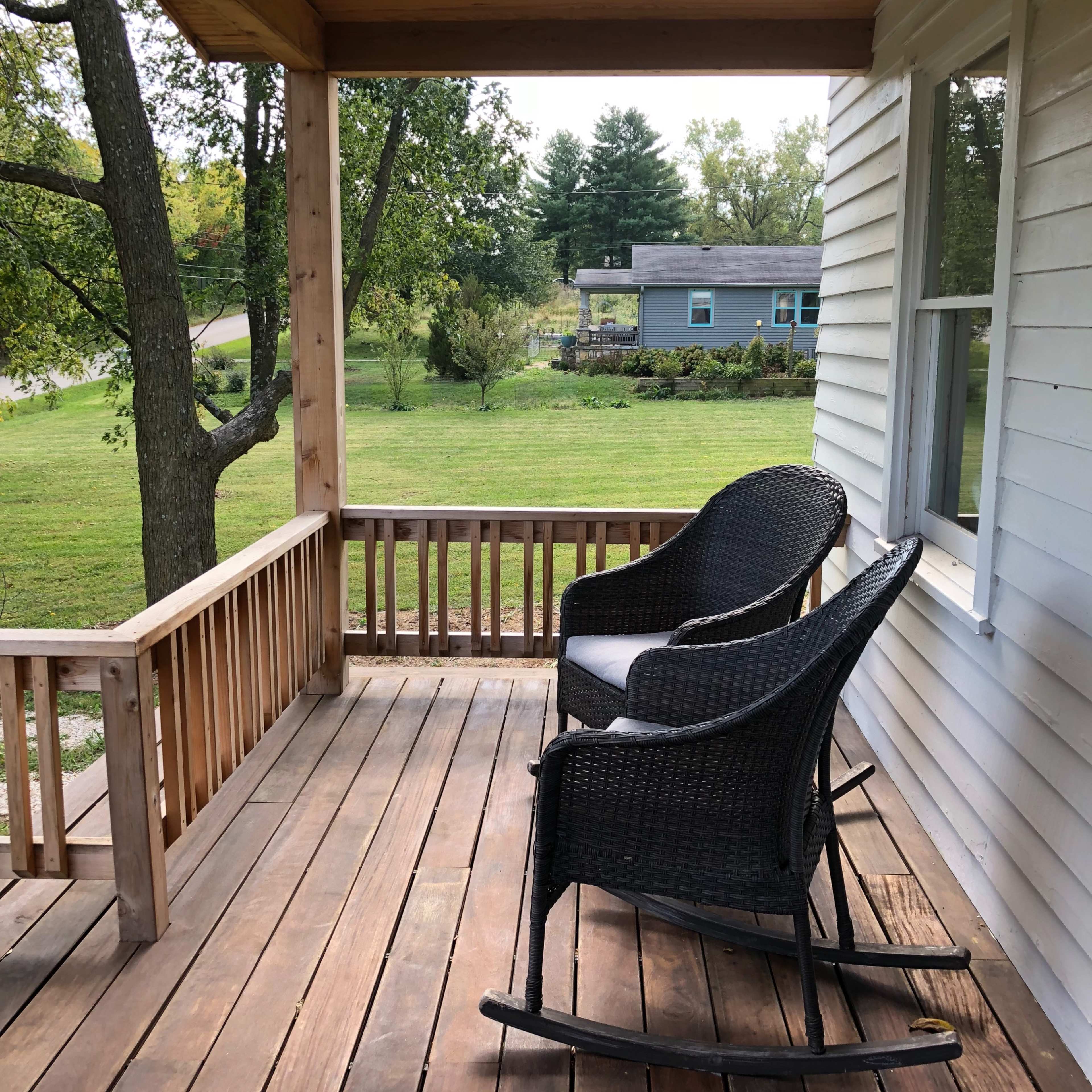 A porch features two rocking chairs overlooking a grassy yard and trees.