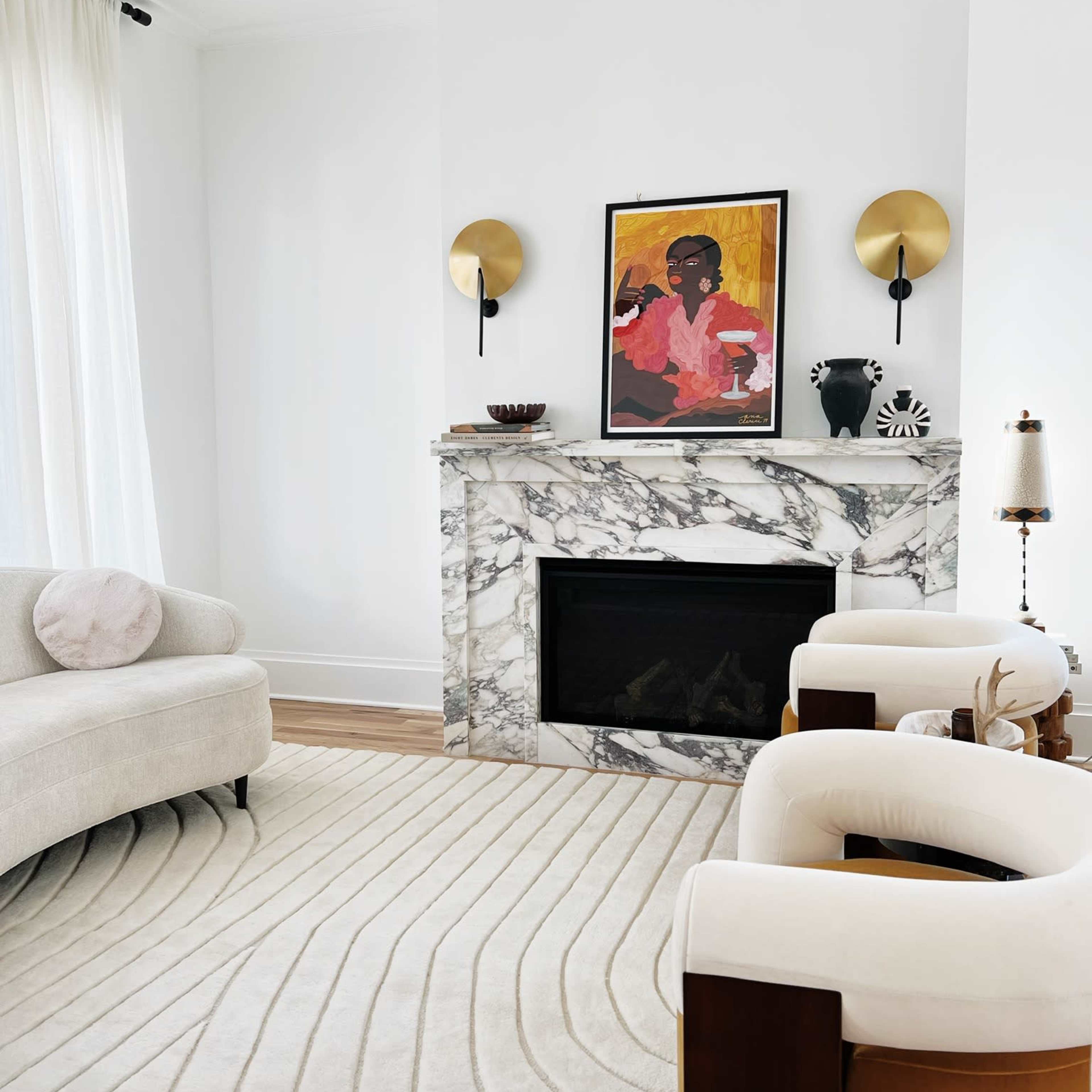 A modern living room featuring a marble fireplace, two upholstered chairs, a curved sofa, and a large area rug with a wavy design.