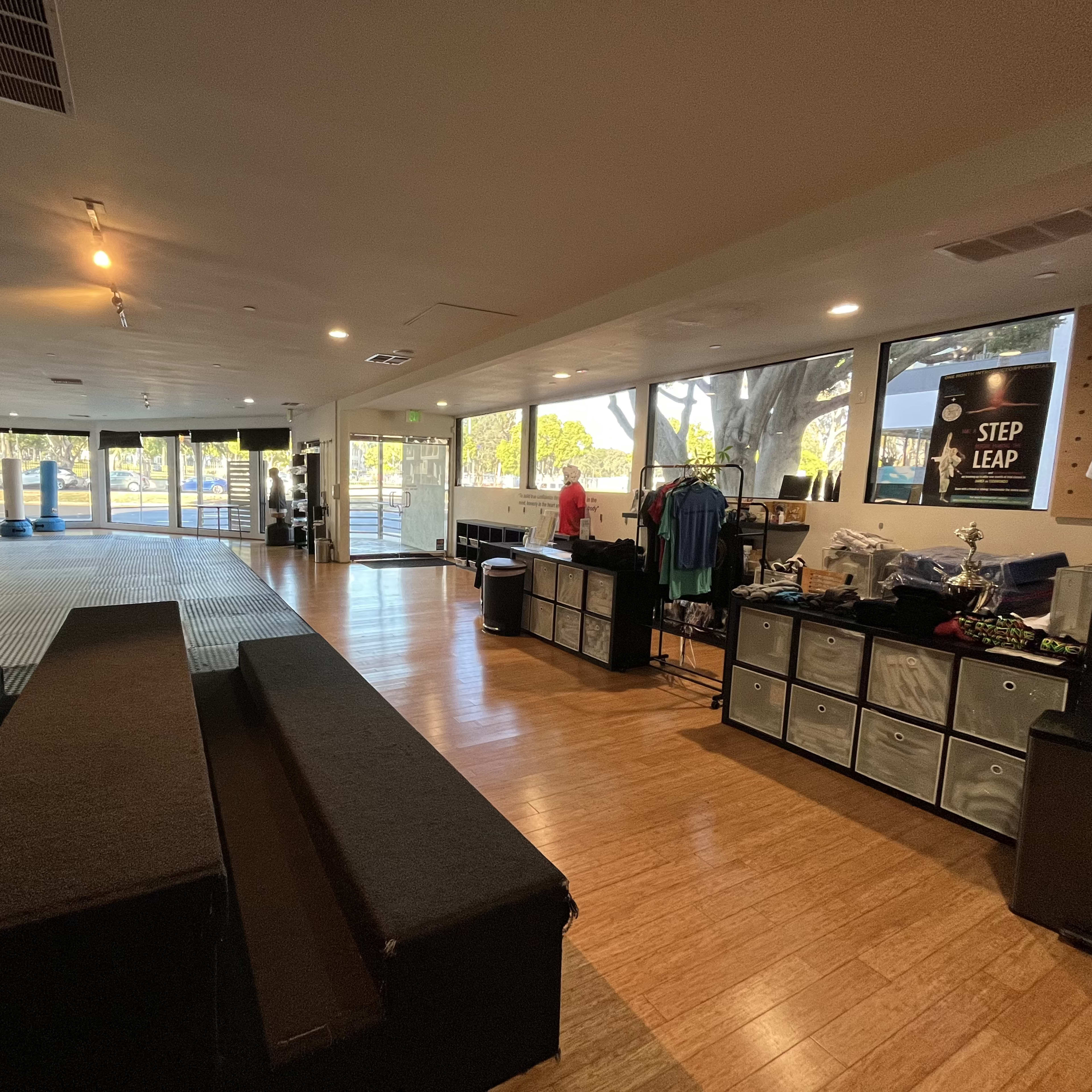 A spacious training facility with mats, benches, and merchandise displays visible near large windows.