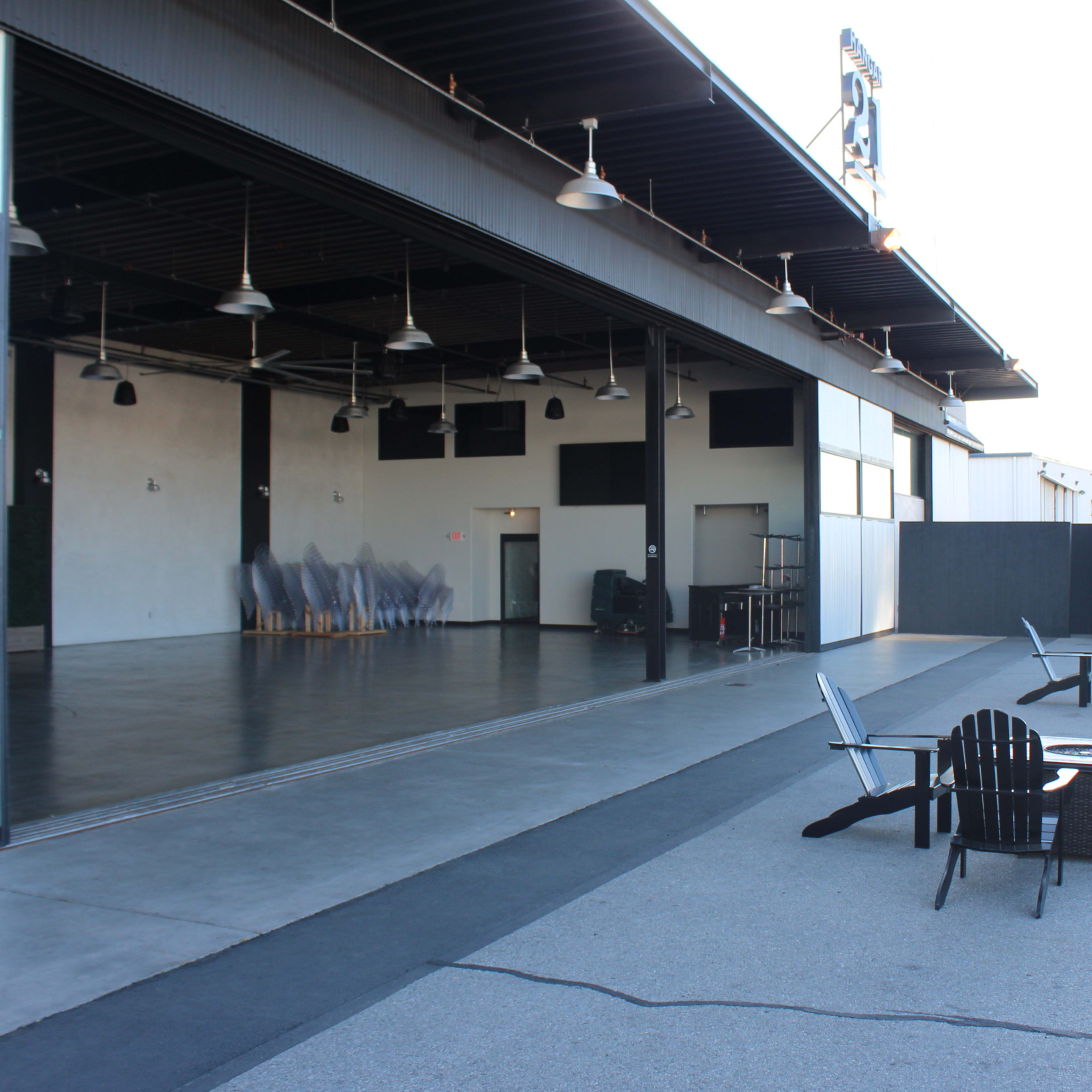 A large, open space with seating areas and a backdrop of a building featuring large glass doors, alongside a bar or service area nearby.