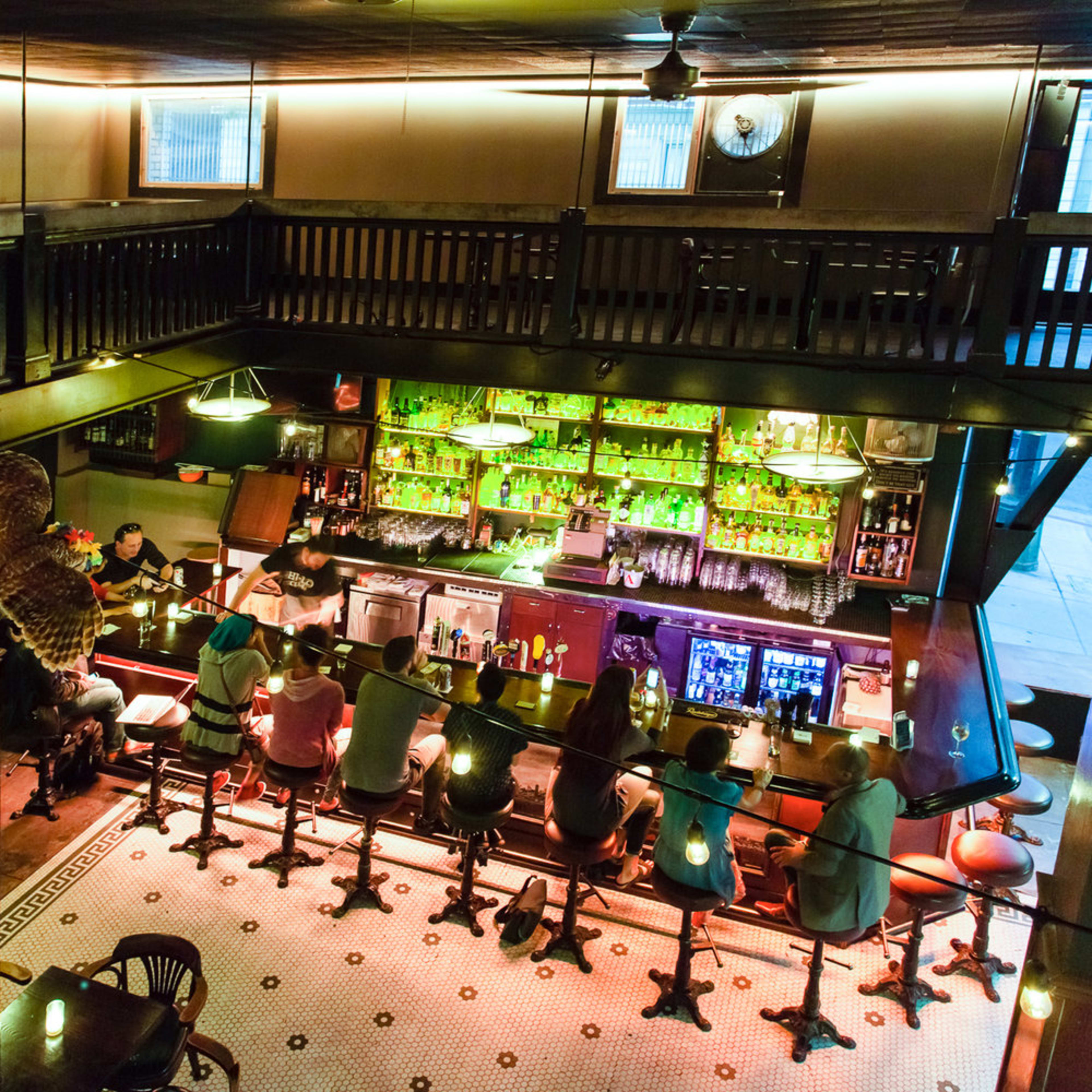 A vibrant bar scene with patrons seated at a counter, surrounded by illuminated shelves filled with various bottles.