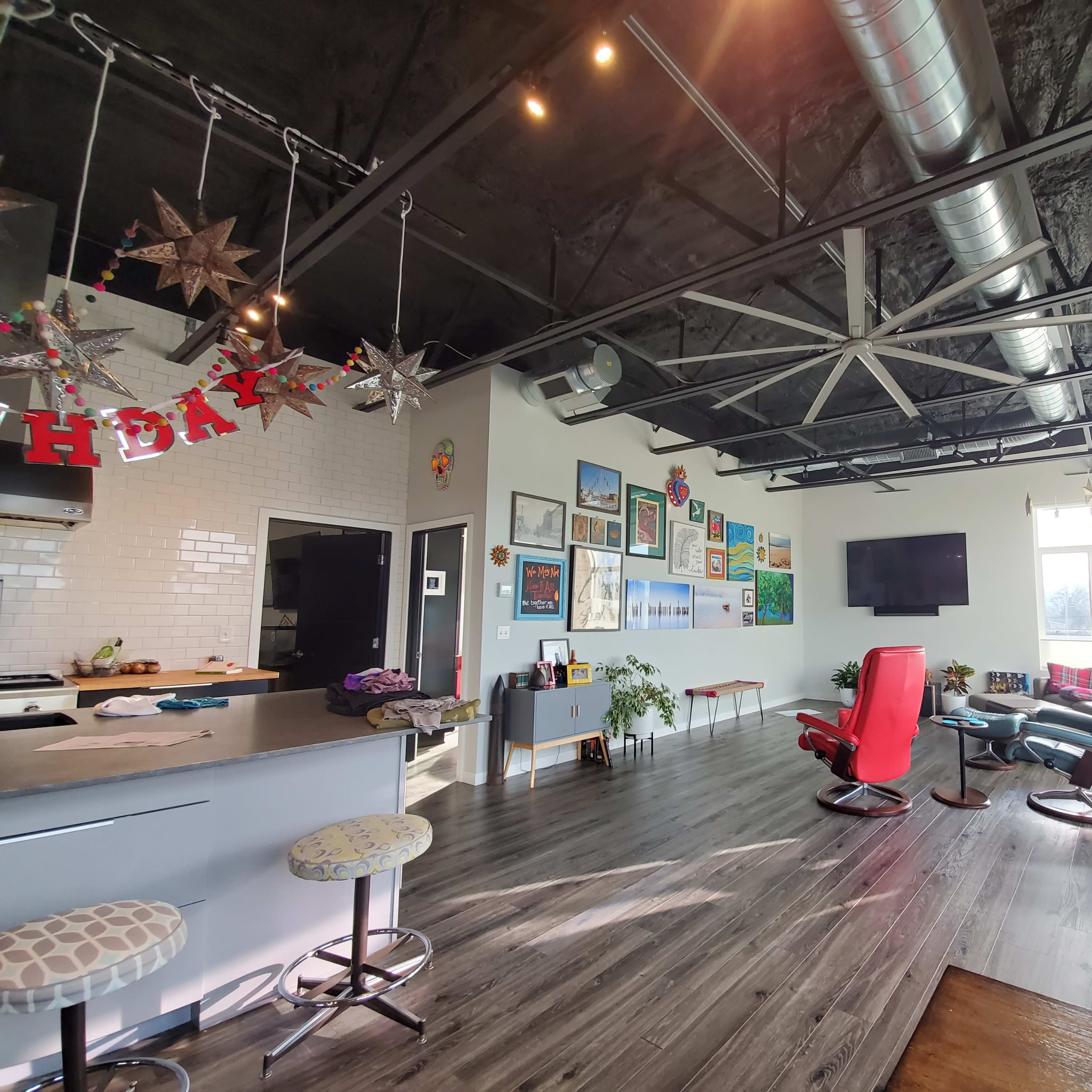A modern open-concept living space with a kitchen area, colorful artwork on the walls, and a mix of seating options including a red recliner and a blue armchair.