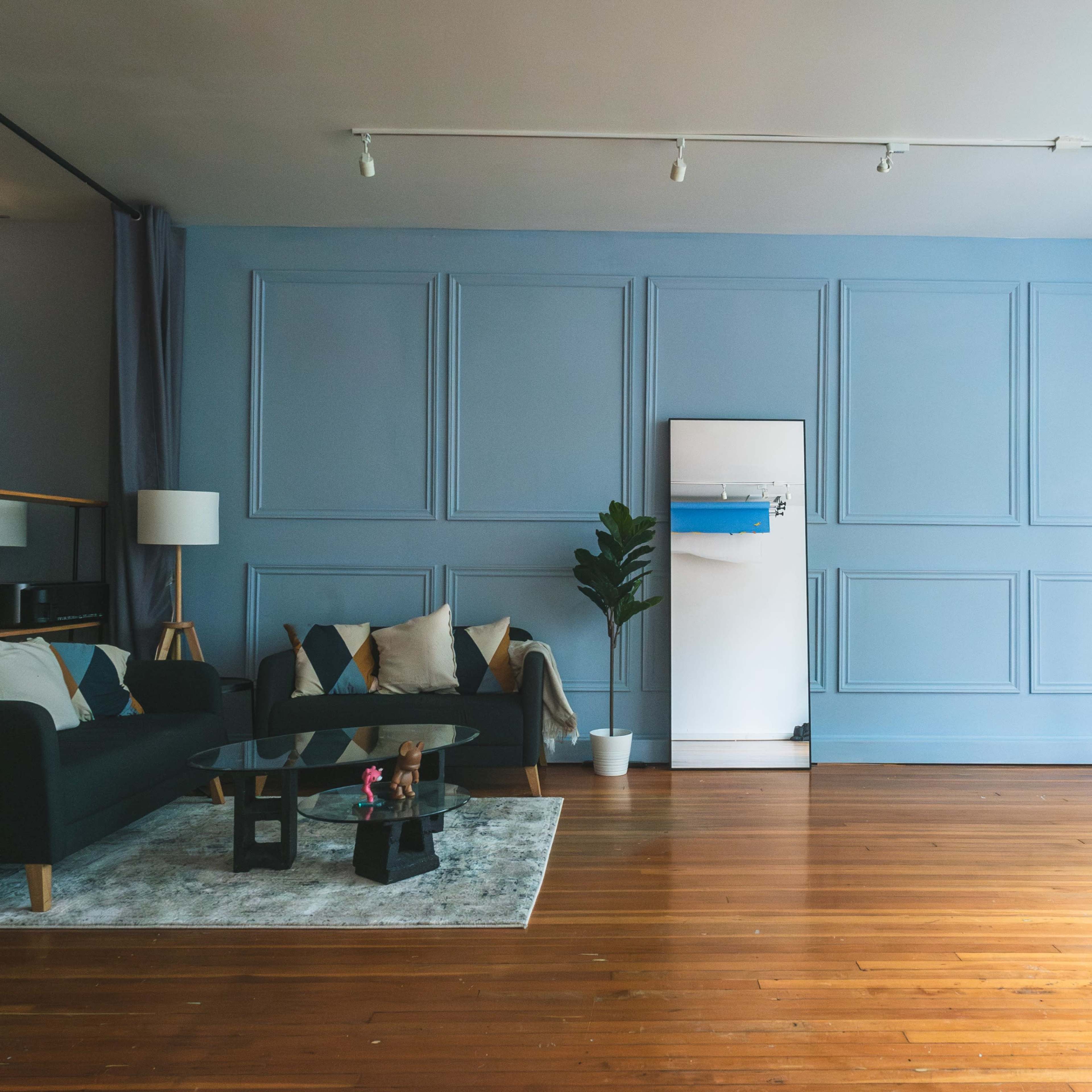 A modern living room with a blue wall, a dark green sofa, a white fridge, and a small plant next to a window.