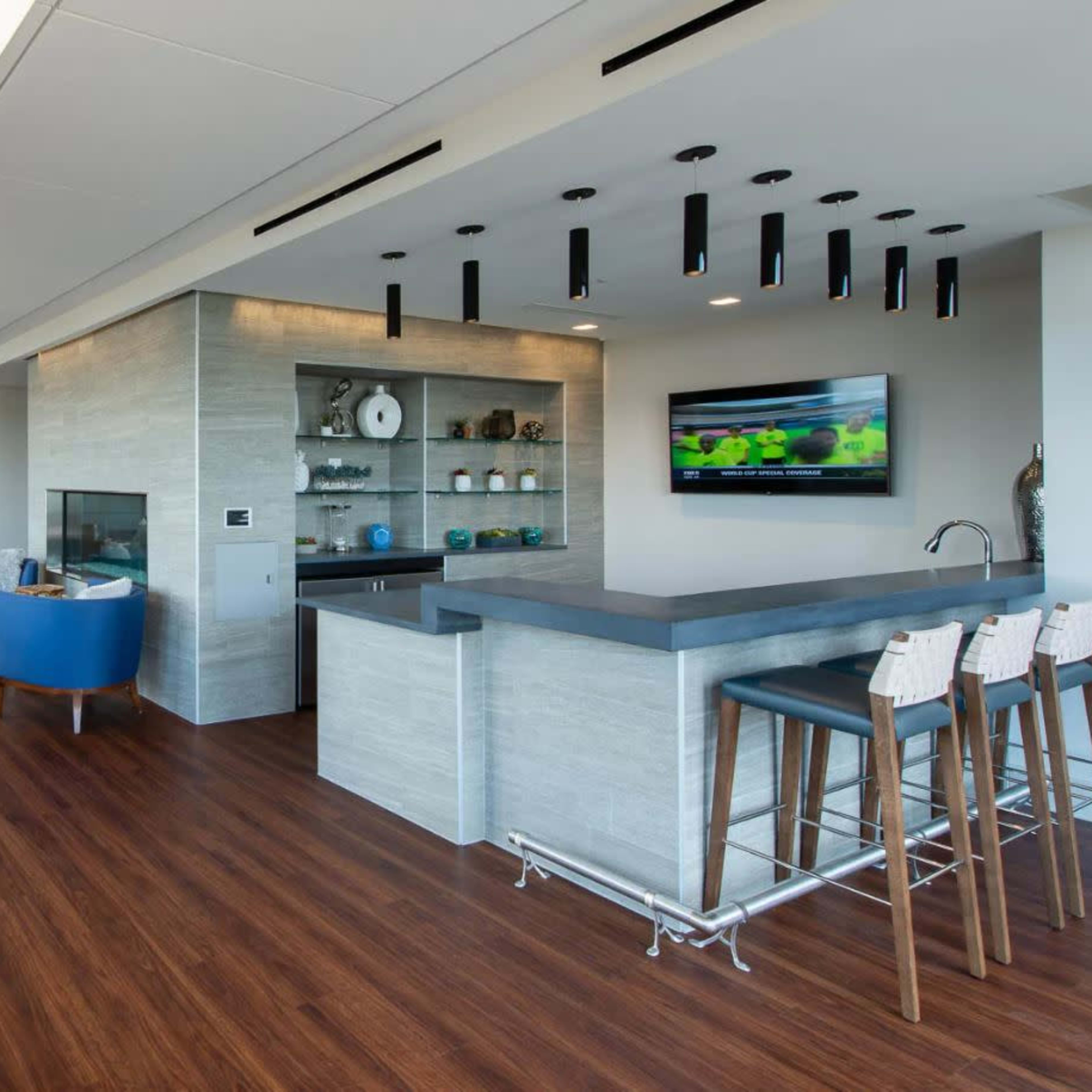 A modern lounge area with a kitchen bar, seating arrangements, and large windows providing ample natural light.