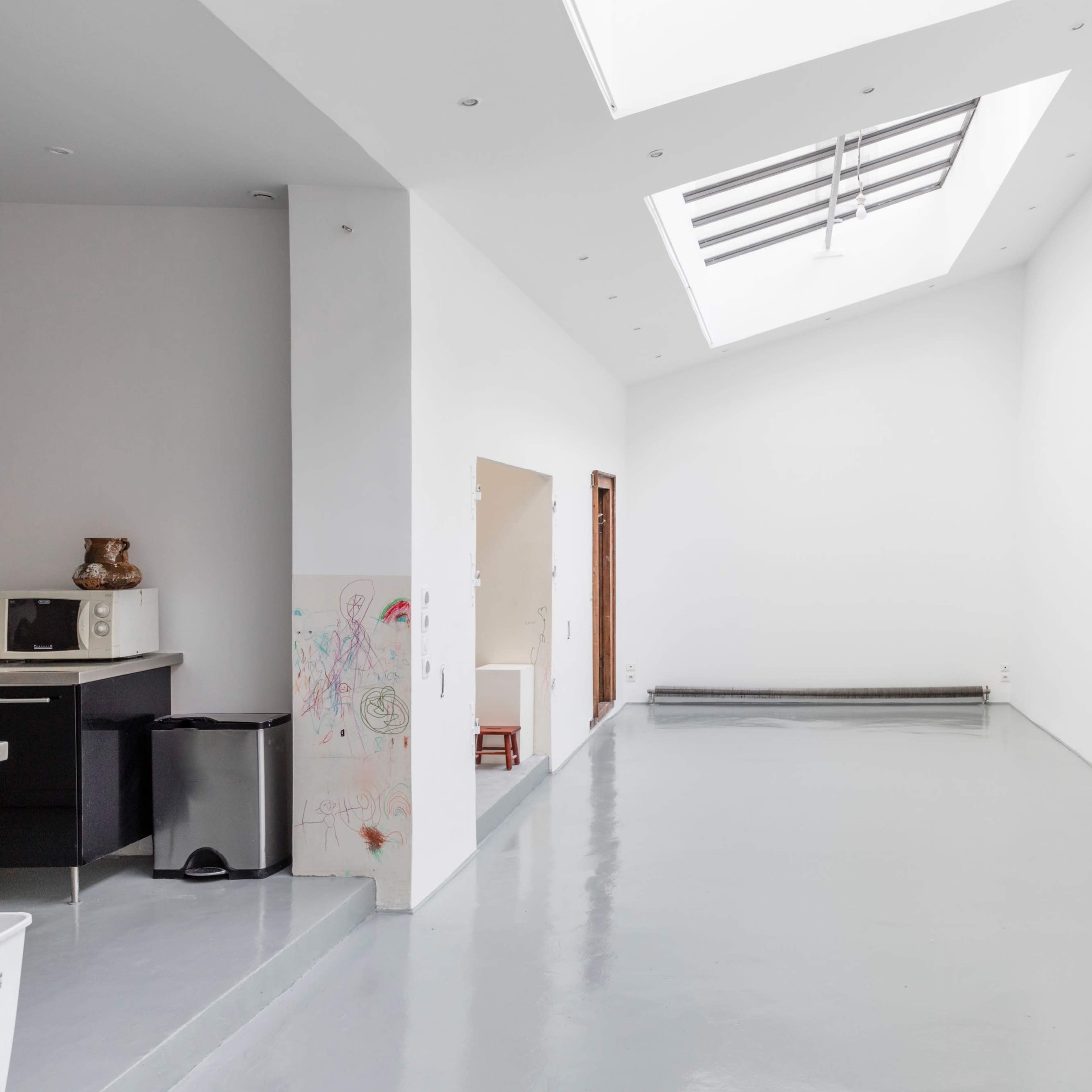 A spacious, empty room with white walls, a skylight, and a polished gray floor.