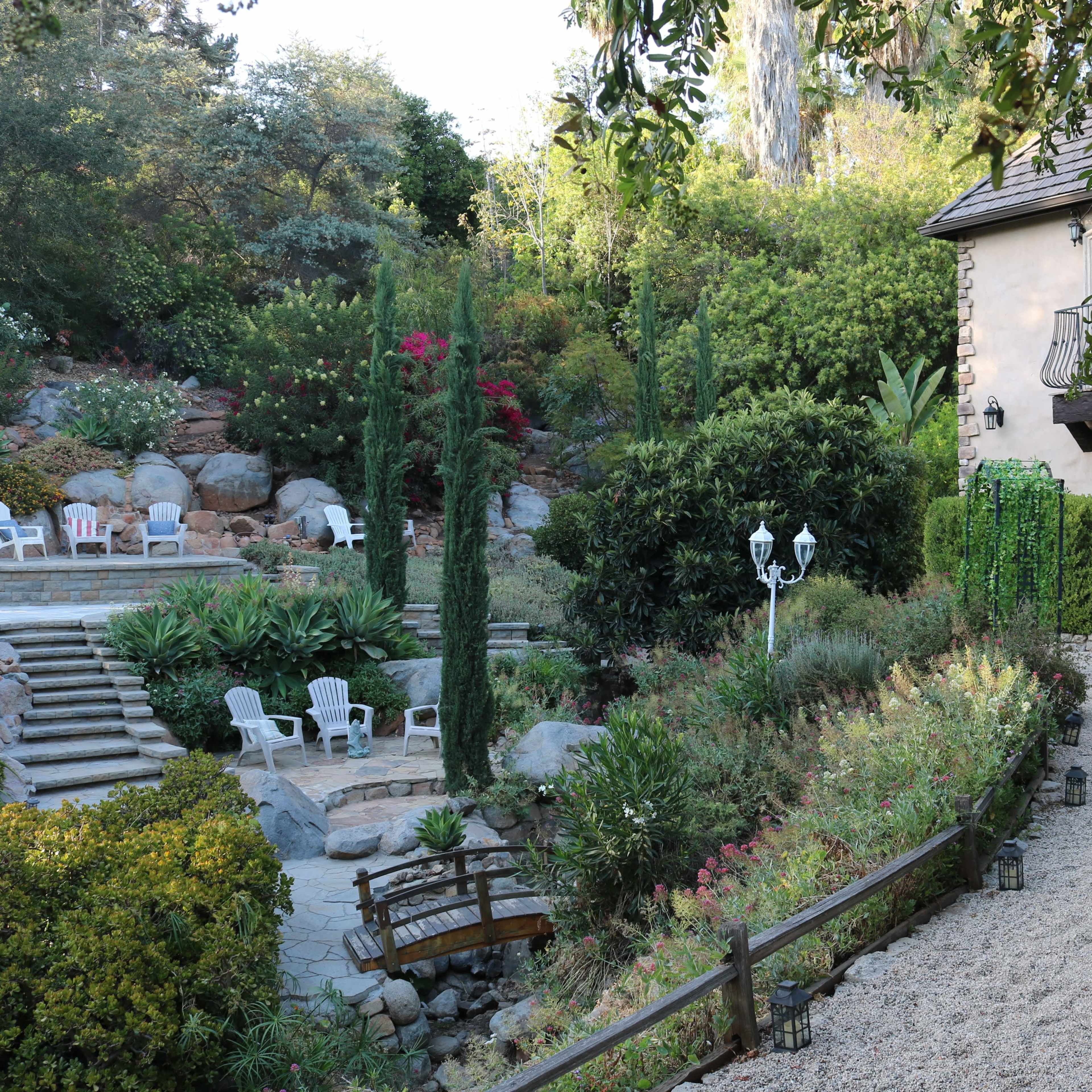 A landscaped garden with pathways, seating areas, and a stone building surrounded by greenery.
