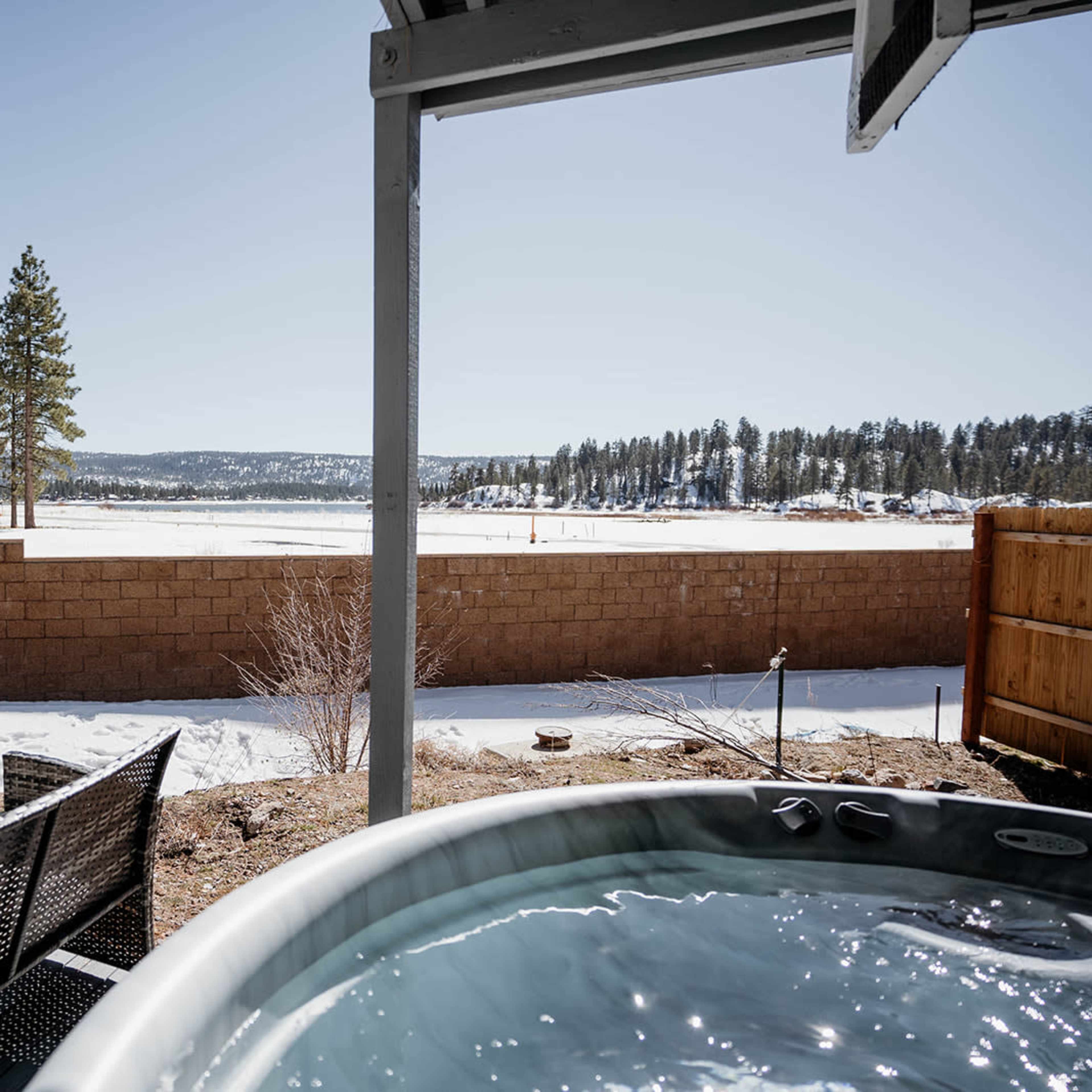 A hot tub overlooks a snowy landscape with a lake and trees in the background.