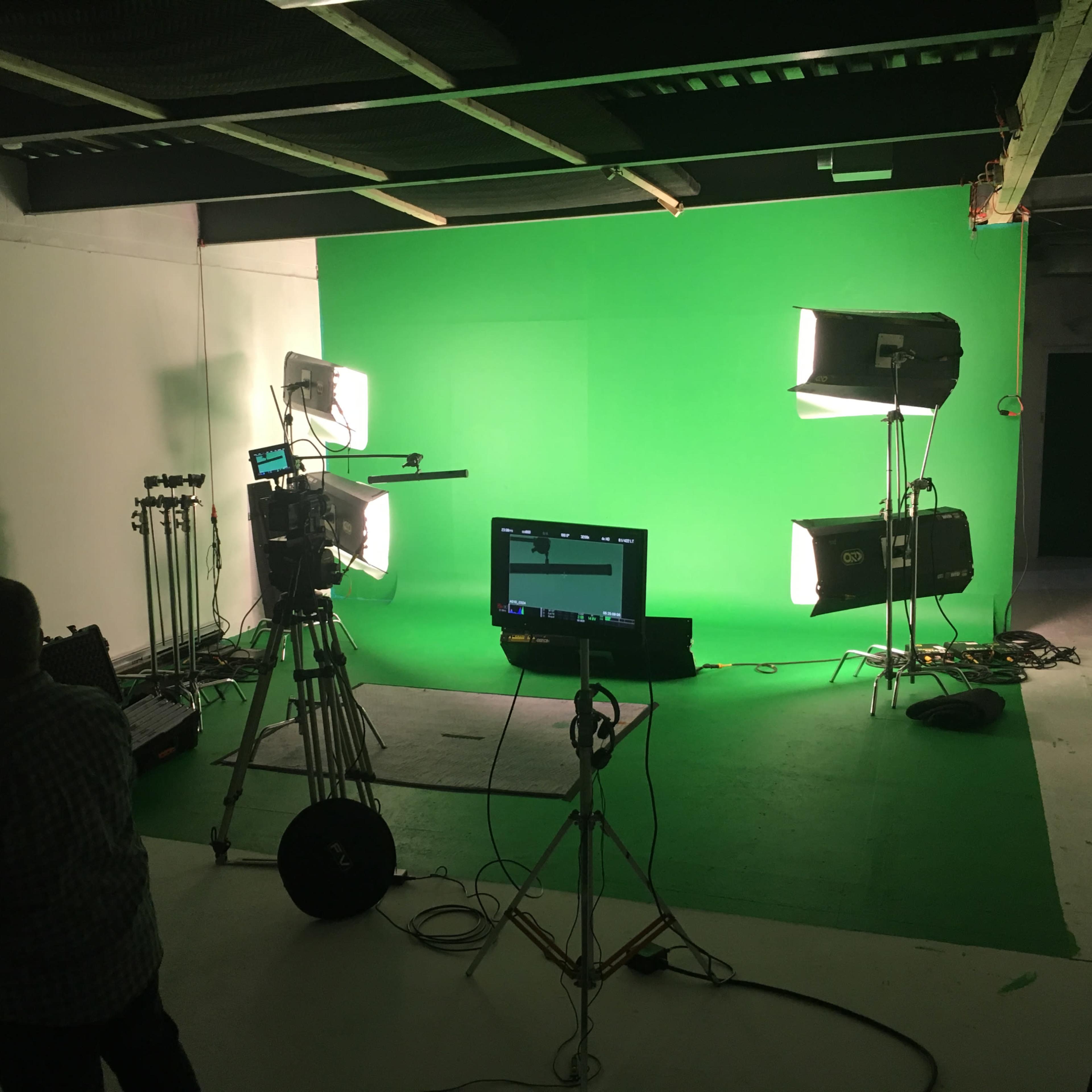 A film studio features a green screen setup with bright lights and a camera on a tripod.