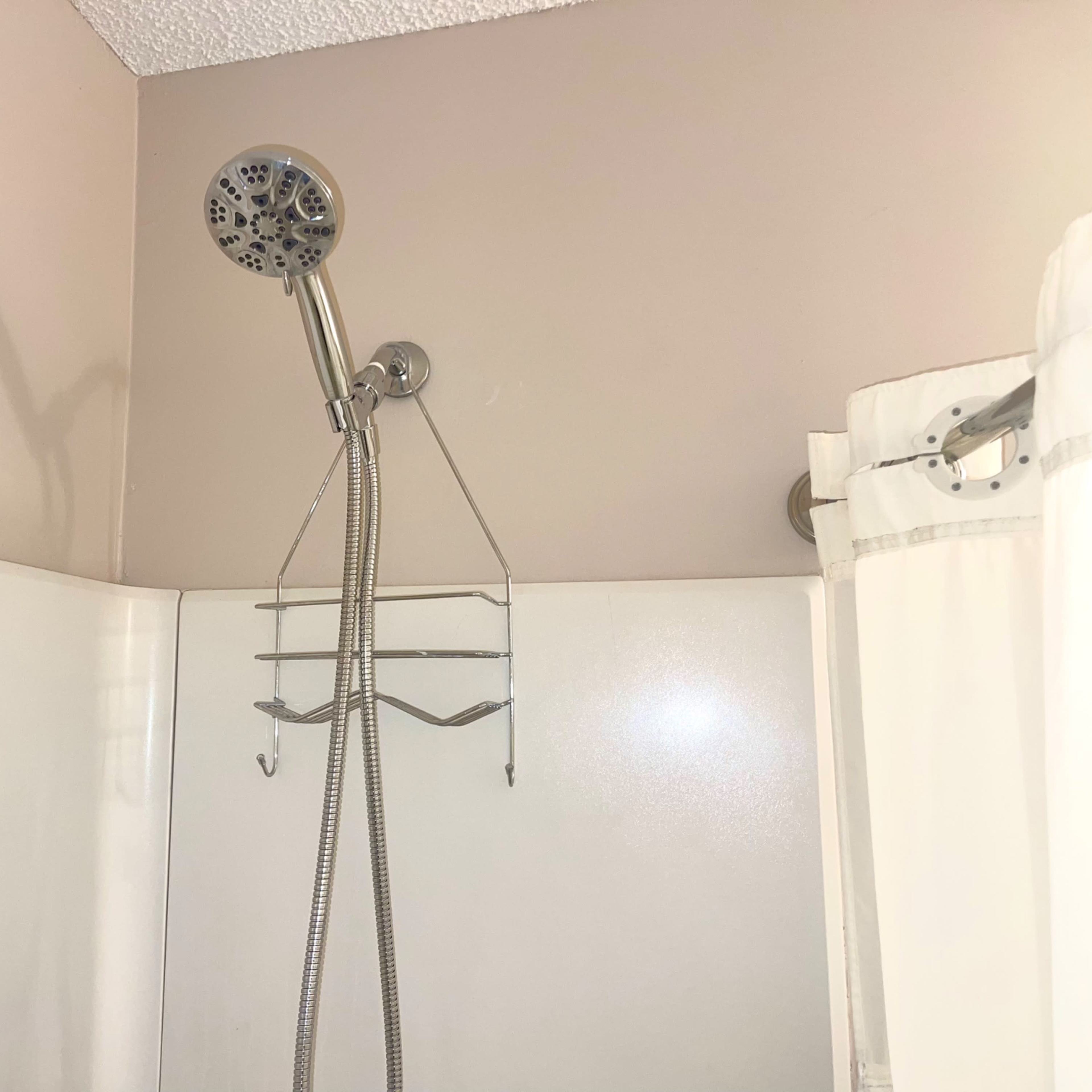 A showerhead mounted on a wall with a flexible hose and a metal caddy for holding items.