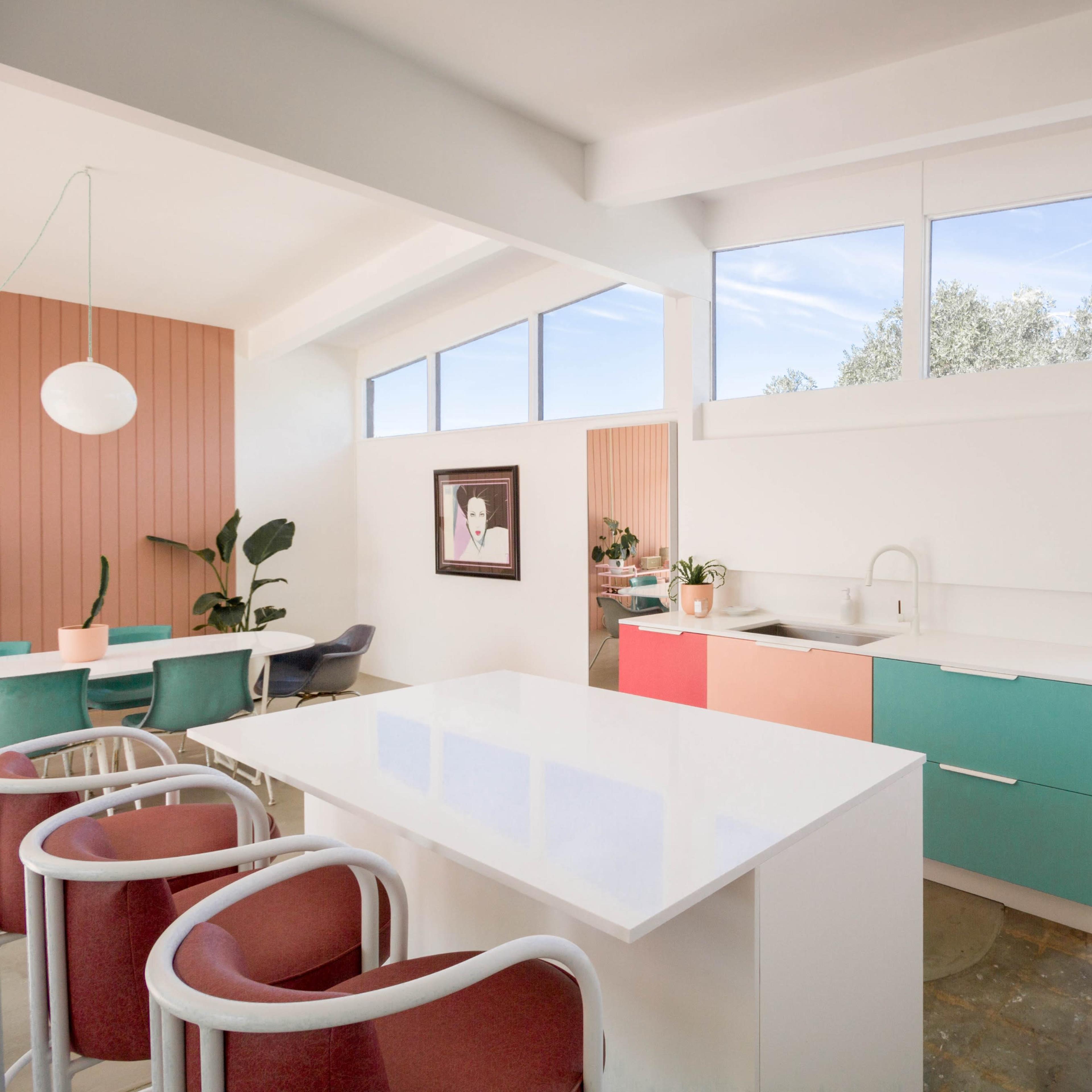 A modern kitchen features colorful cabinets, a sleek white countertop, and large windows that allow natural light to fill the space.