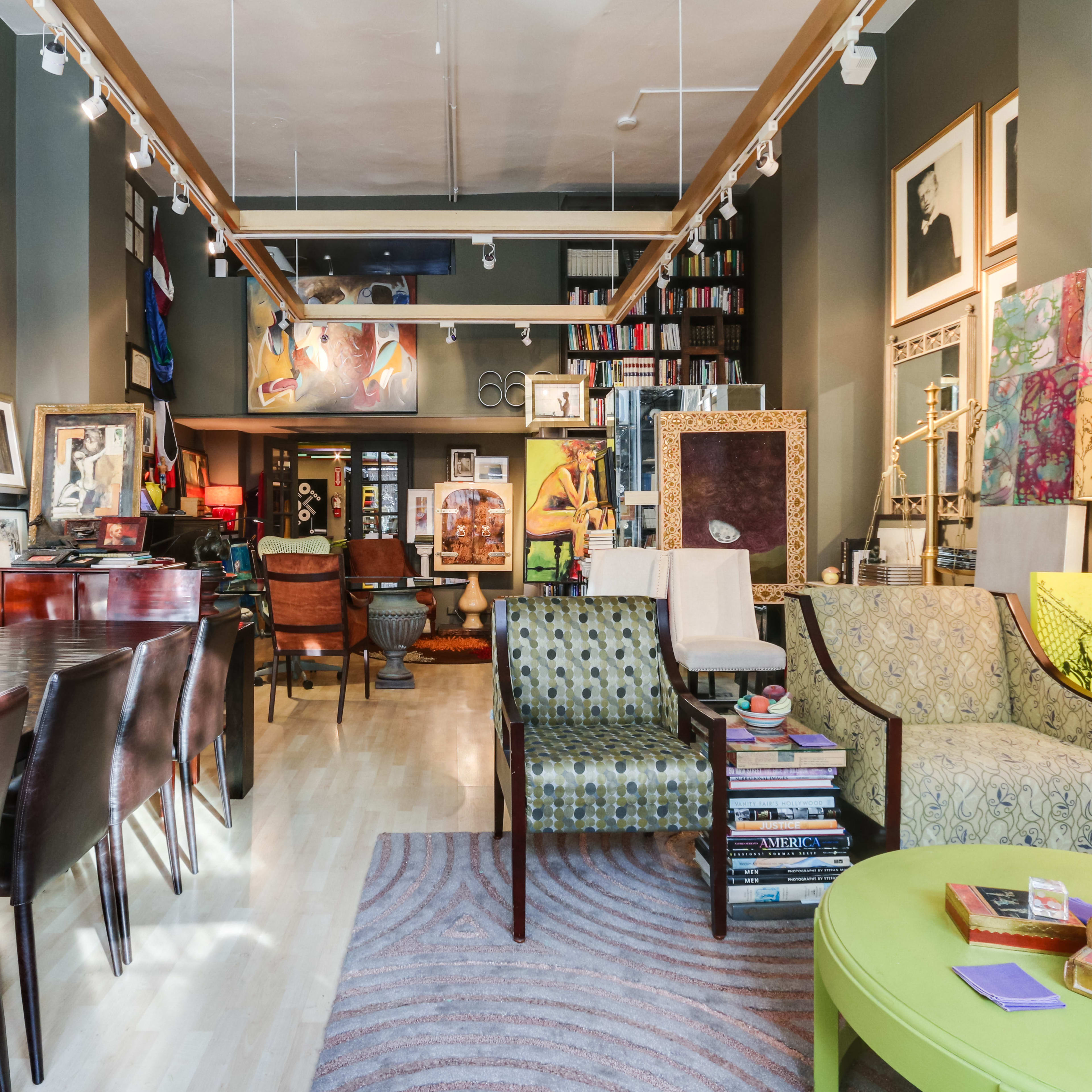 An art-focused interior space featuring a mix of framed photographs and paintings on the walls, various seating arrangements, and a long dining table.