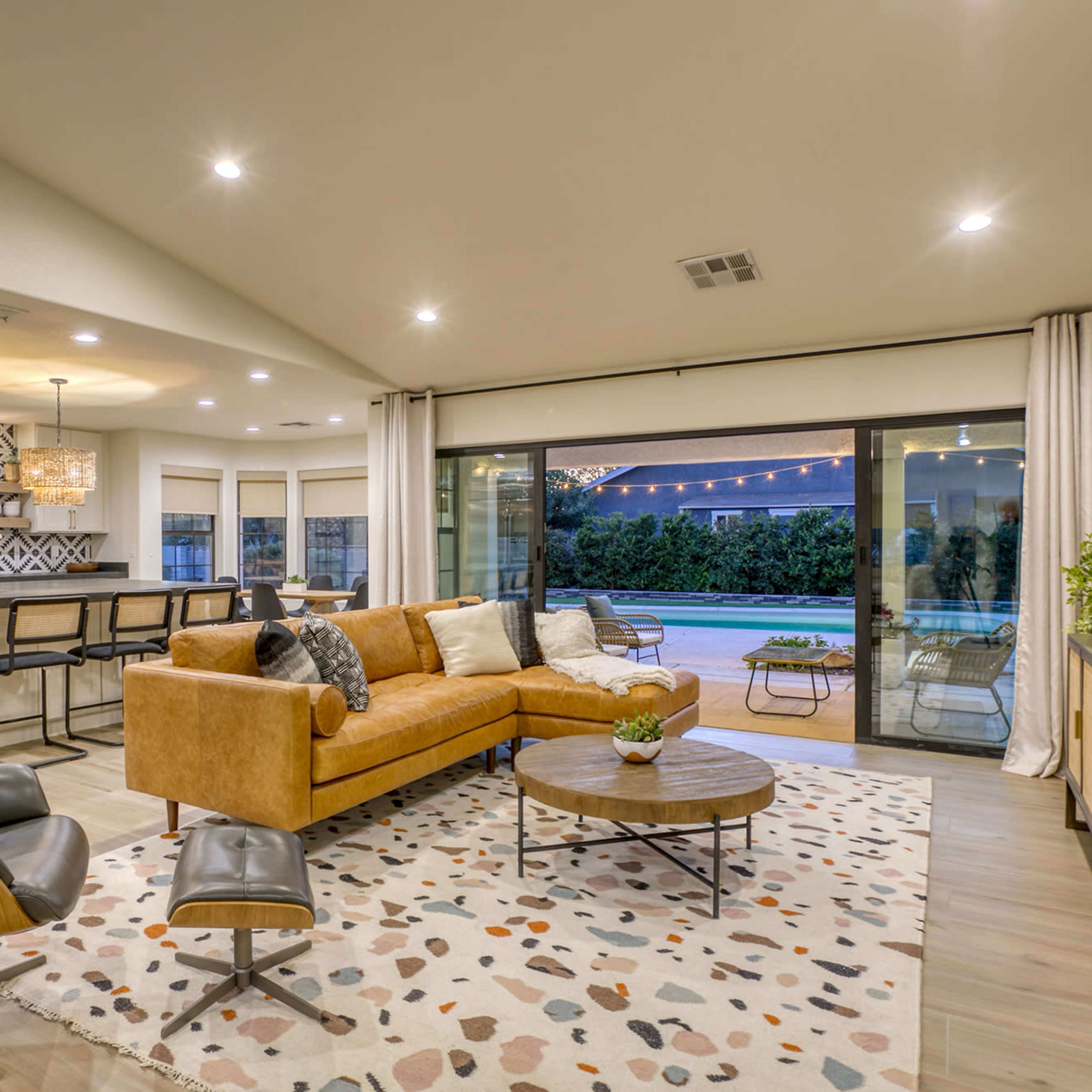 A modern living room with a brown leather sofa, a circular wooden coffee table, and large sliding glass doors that open to a patio area.