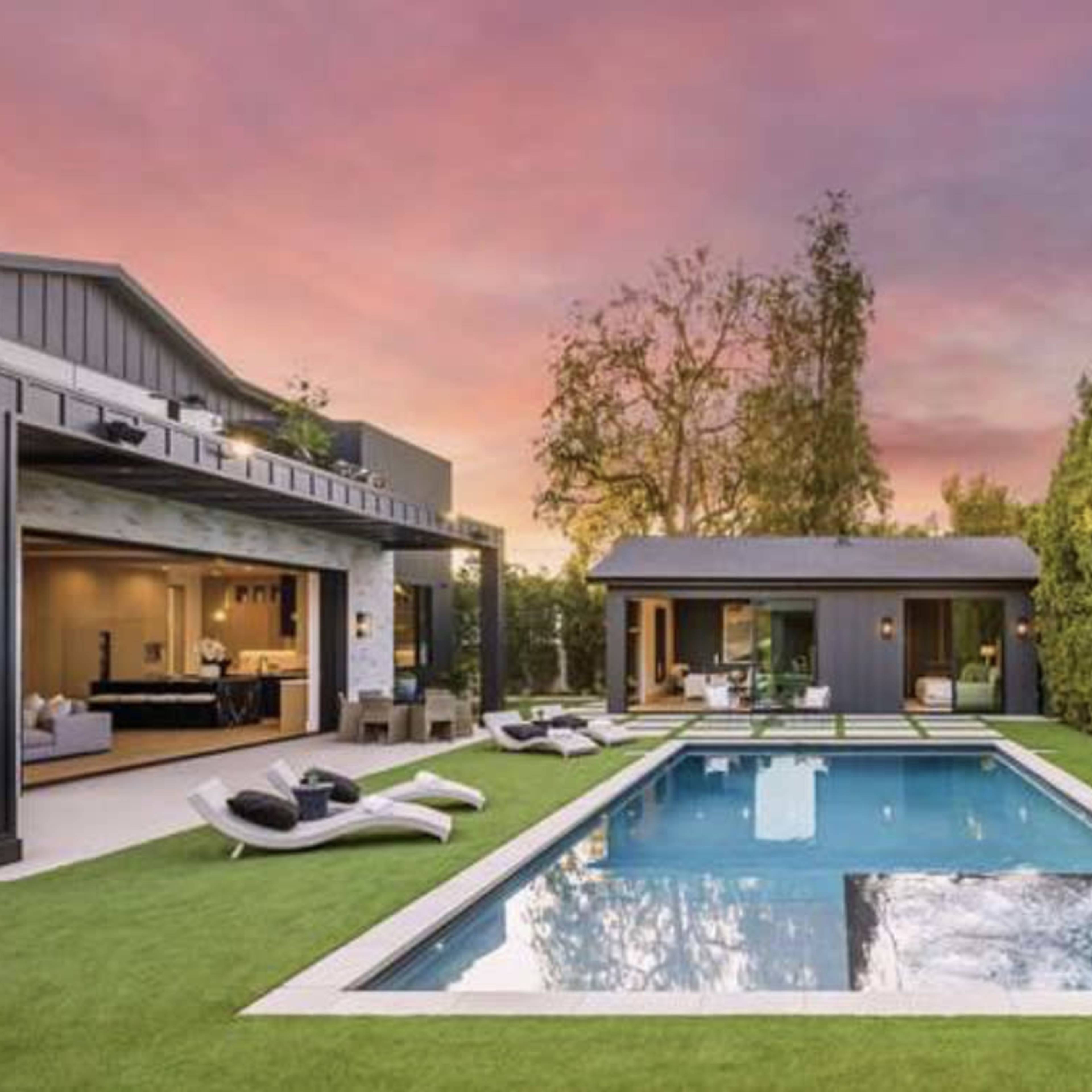 A modern backyard featuring a rectangular swimming pool surrounded by landscaped grass and lounge chairs, with a stylish home in the background against a colorful sunset sky.