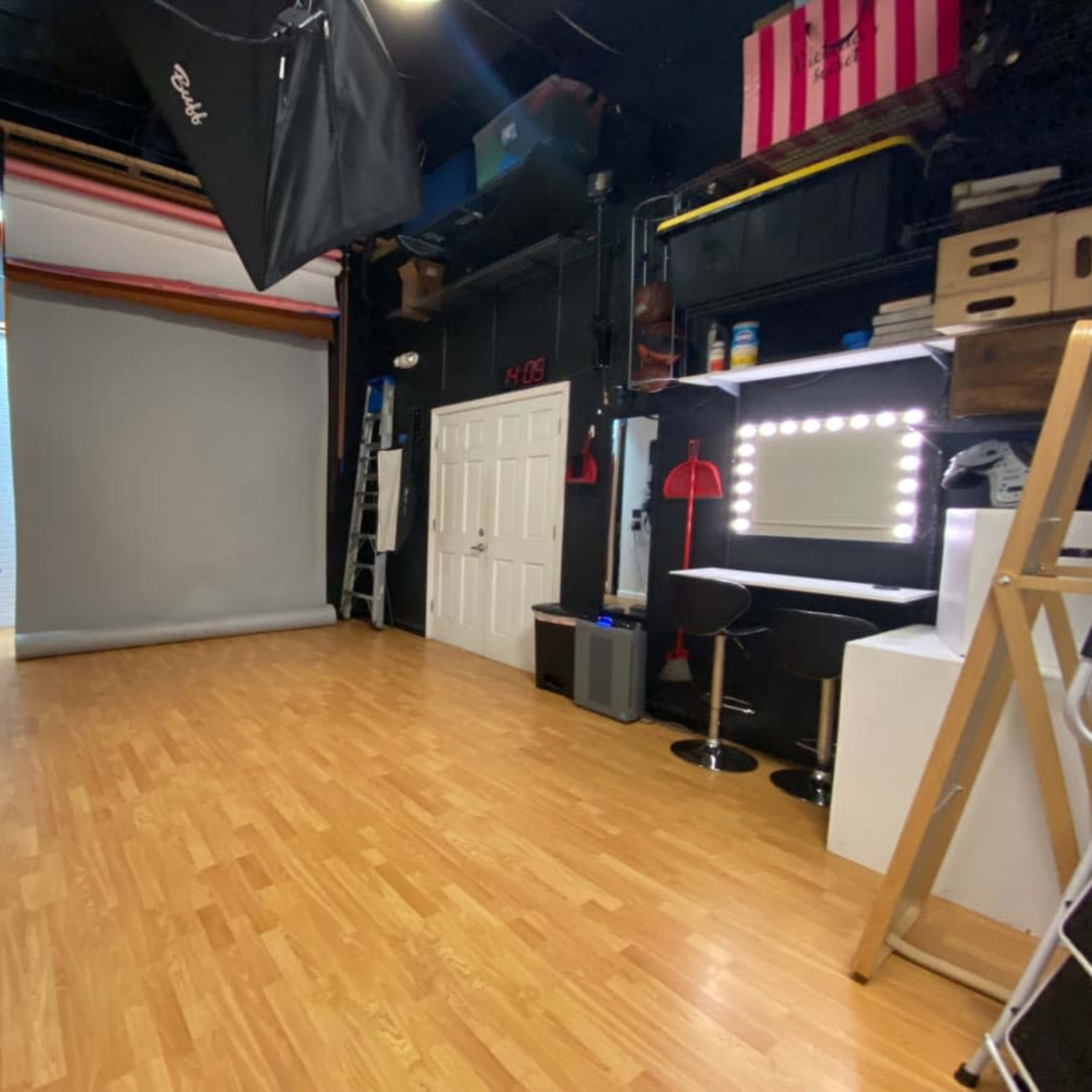 A photography studio with wooden flooring, a grey backdrop, and various lighting equipment along the walls.