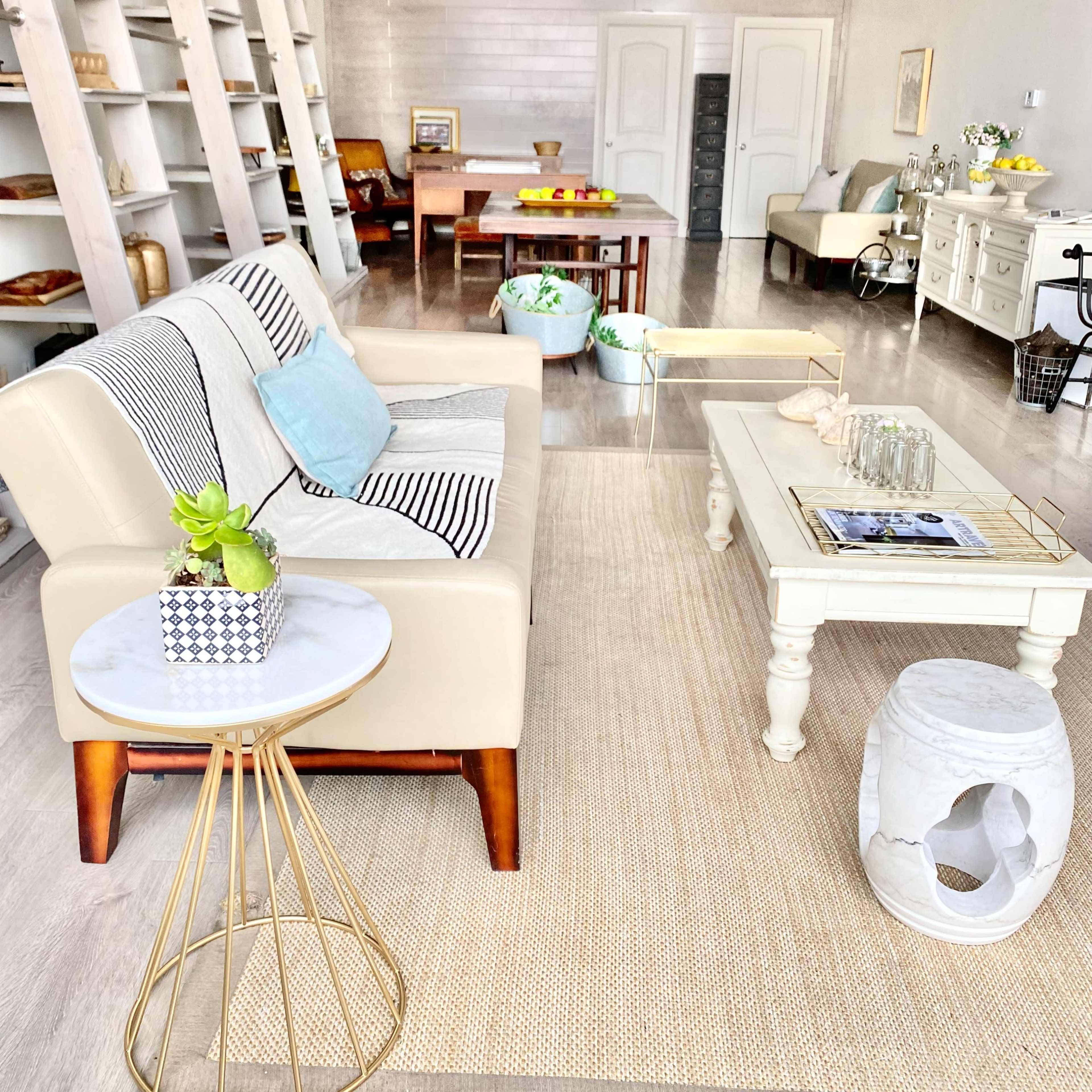 A light and airy living room with a cream-colored sofa, a small coffee table, and wooden shelving holding various decor items.
