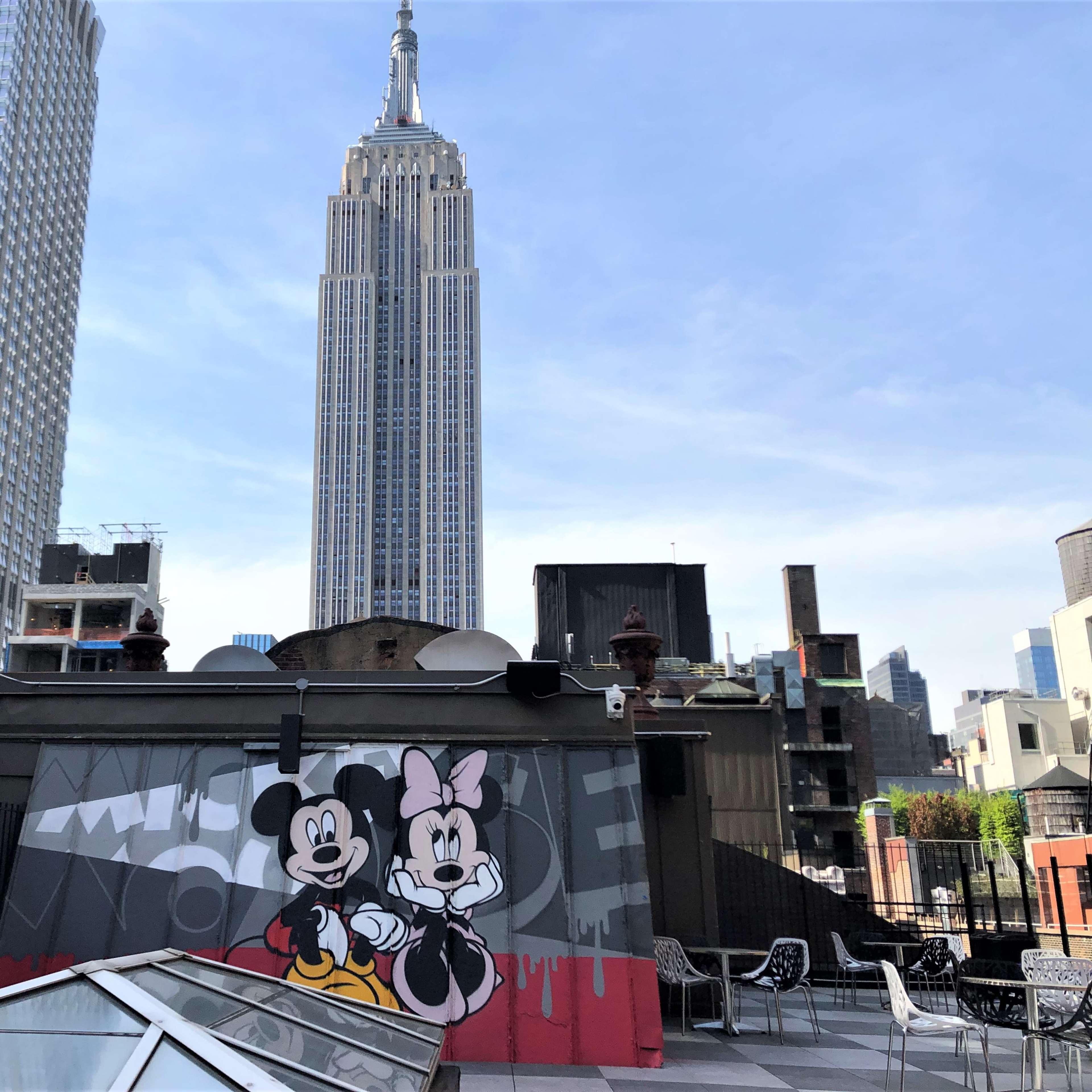 A rooftop featuring a mural of Mickey and Minnie Mouse with the Empire State Building visible in the background.