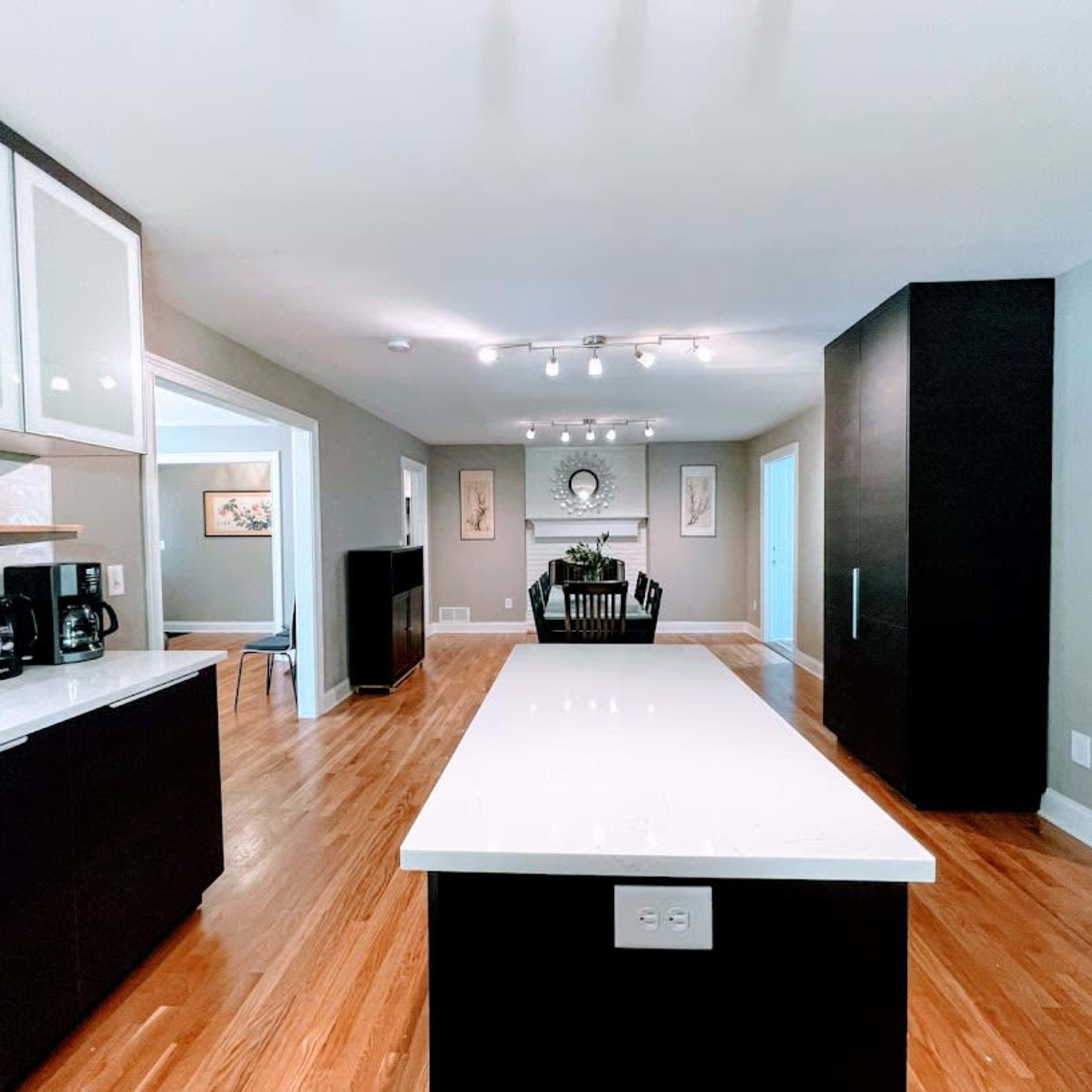 A modern kitchen featuring a central island, dark cabinetry, and a dining area visible in the background.