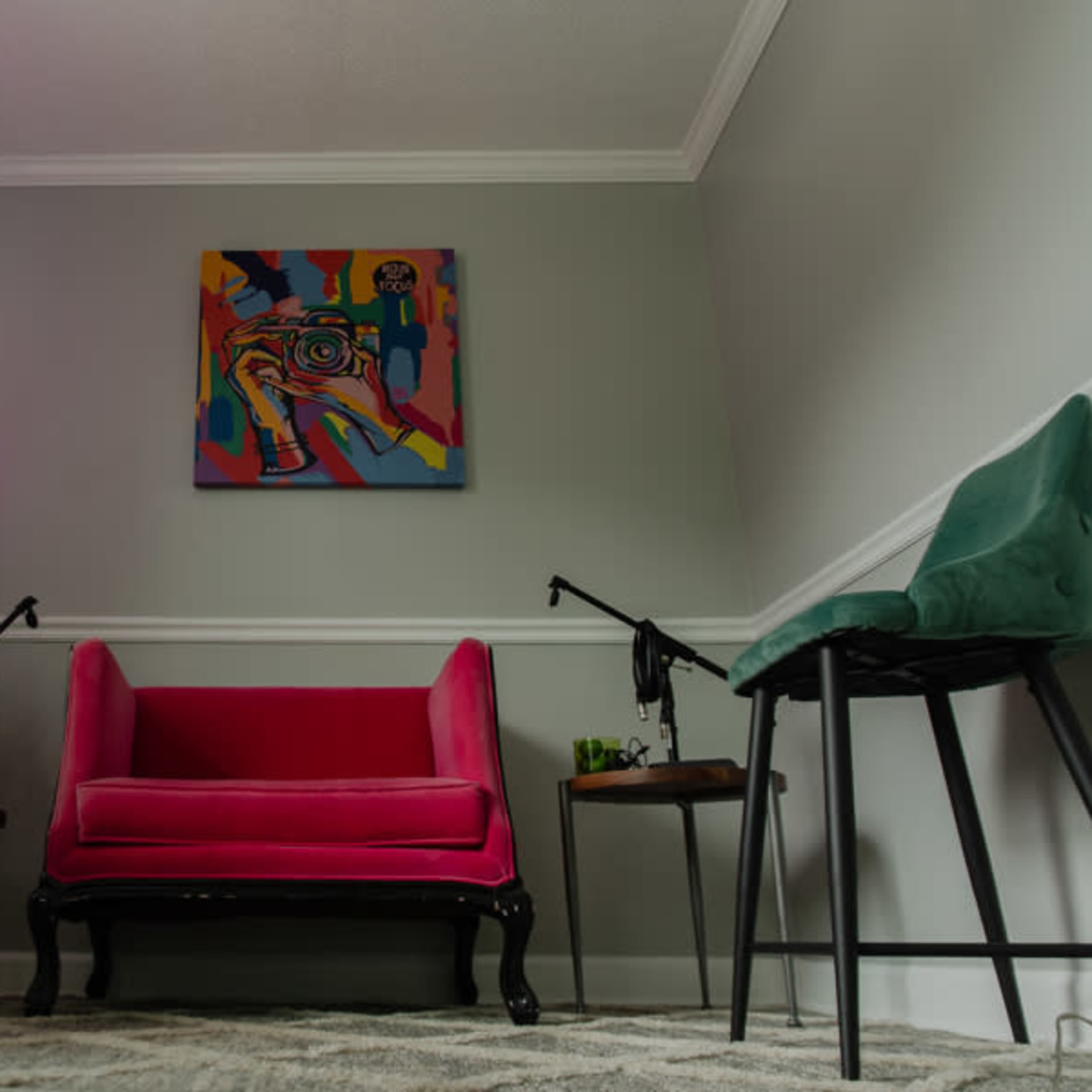 A pink couch is centered in a small room decorated with colorful artwork, flanked by two green chairs and lamps on either side.